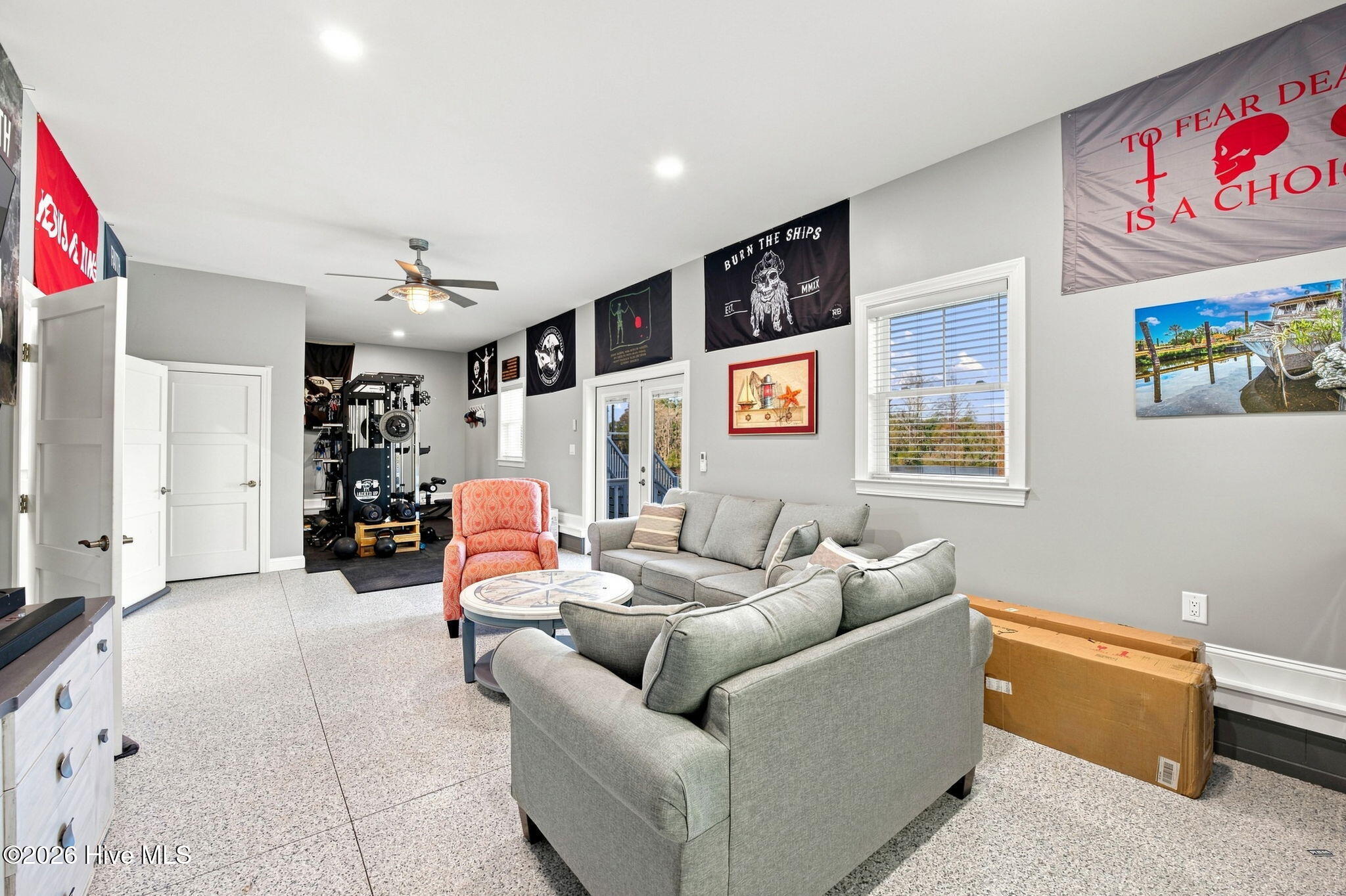 Living room with gray sofas and coral chair beside a home gym with exercise equipment.