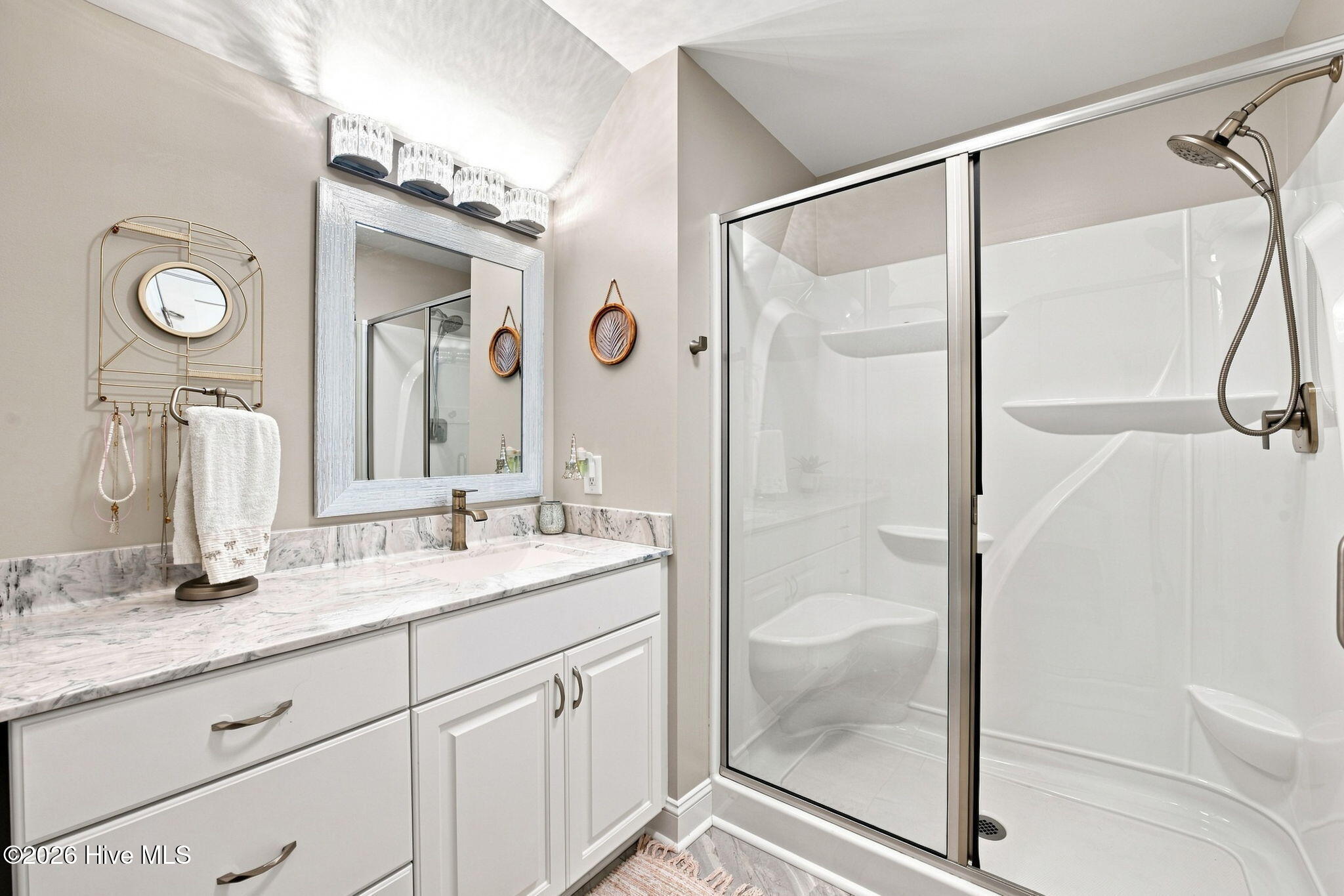 Bathroom with a veined marble vanity and glass-enclosed shower with built-in shelves.