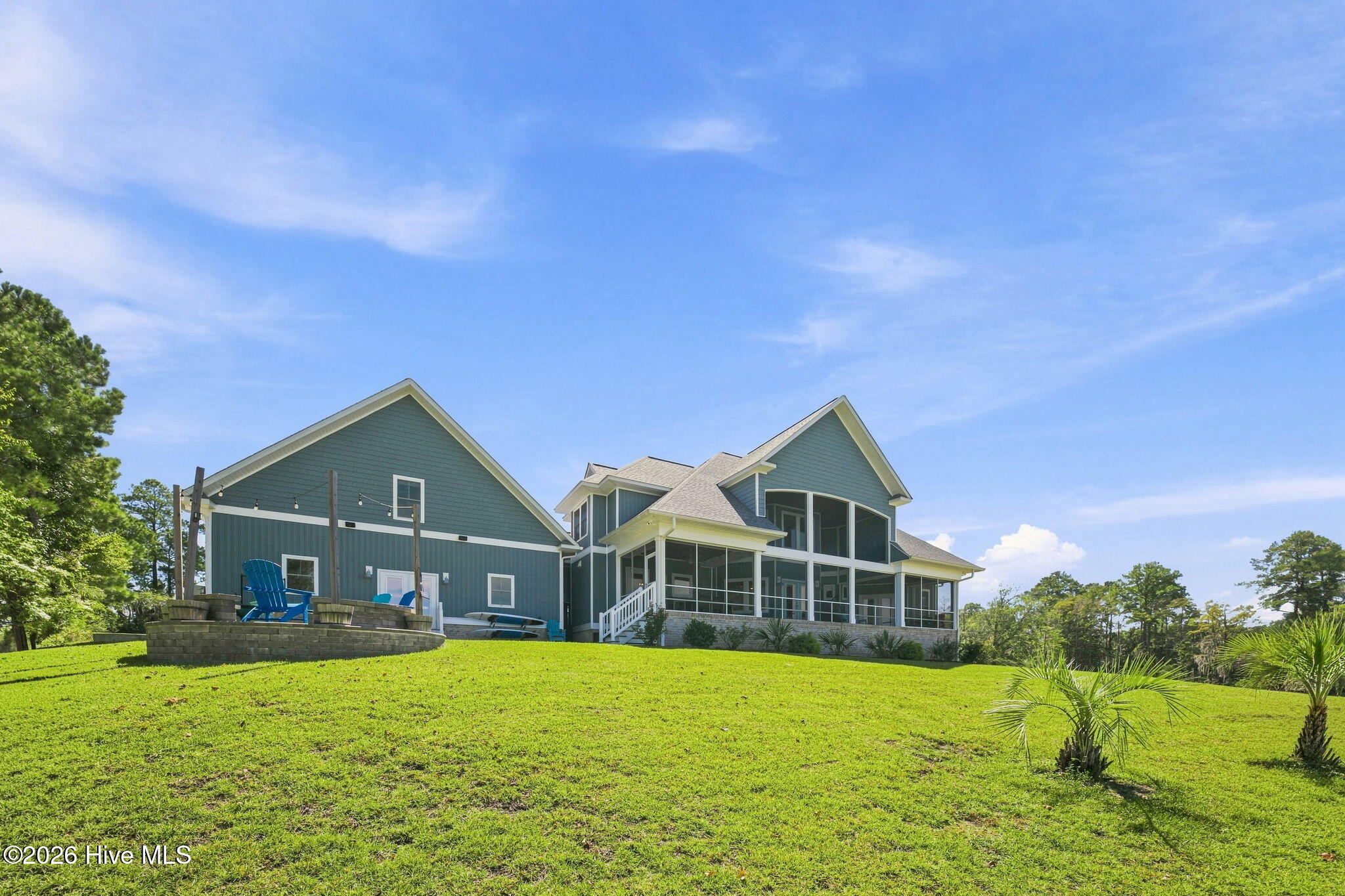 Blue-gray two-story home with a screened porch, raised patio, and broad green lawn.