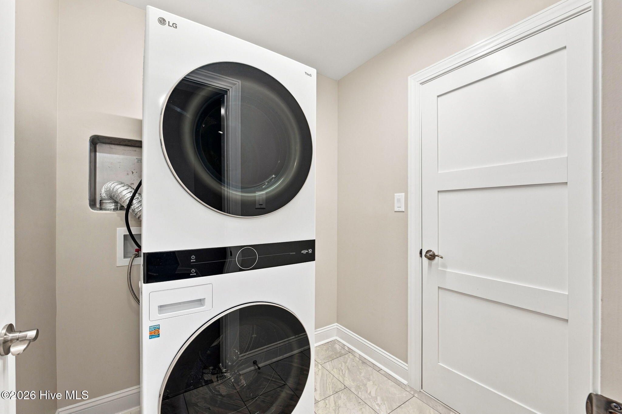 Laundry room with a stacked white washer and dryer beside a paneled door.
