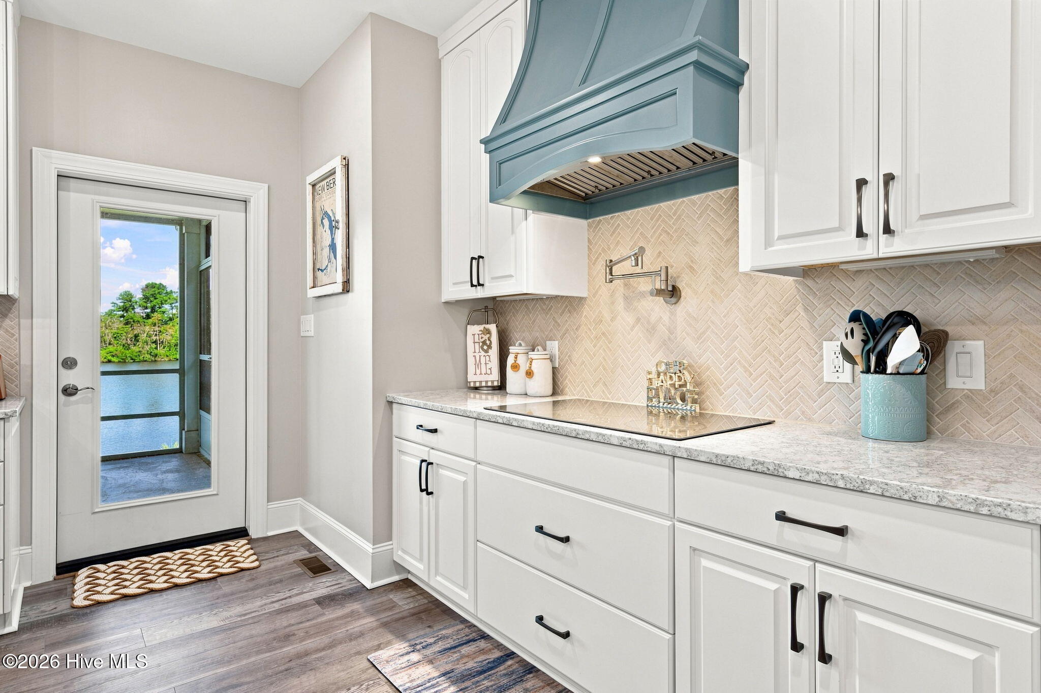 Kitchen with white cabinets and blue range hood; glass door opens to a water view.