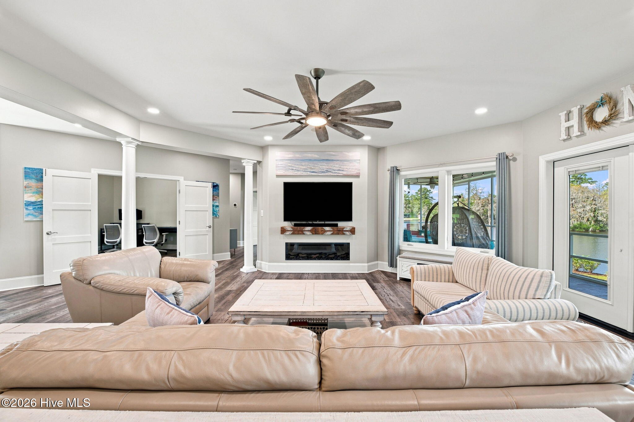 Furnished living room with leather sofas, a TV over the fireplace, and water visible through the glass doors.