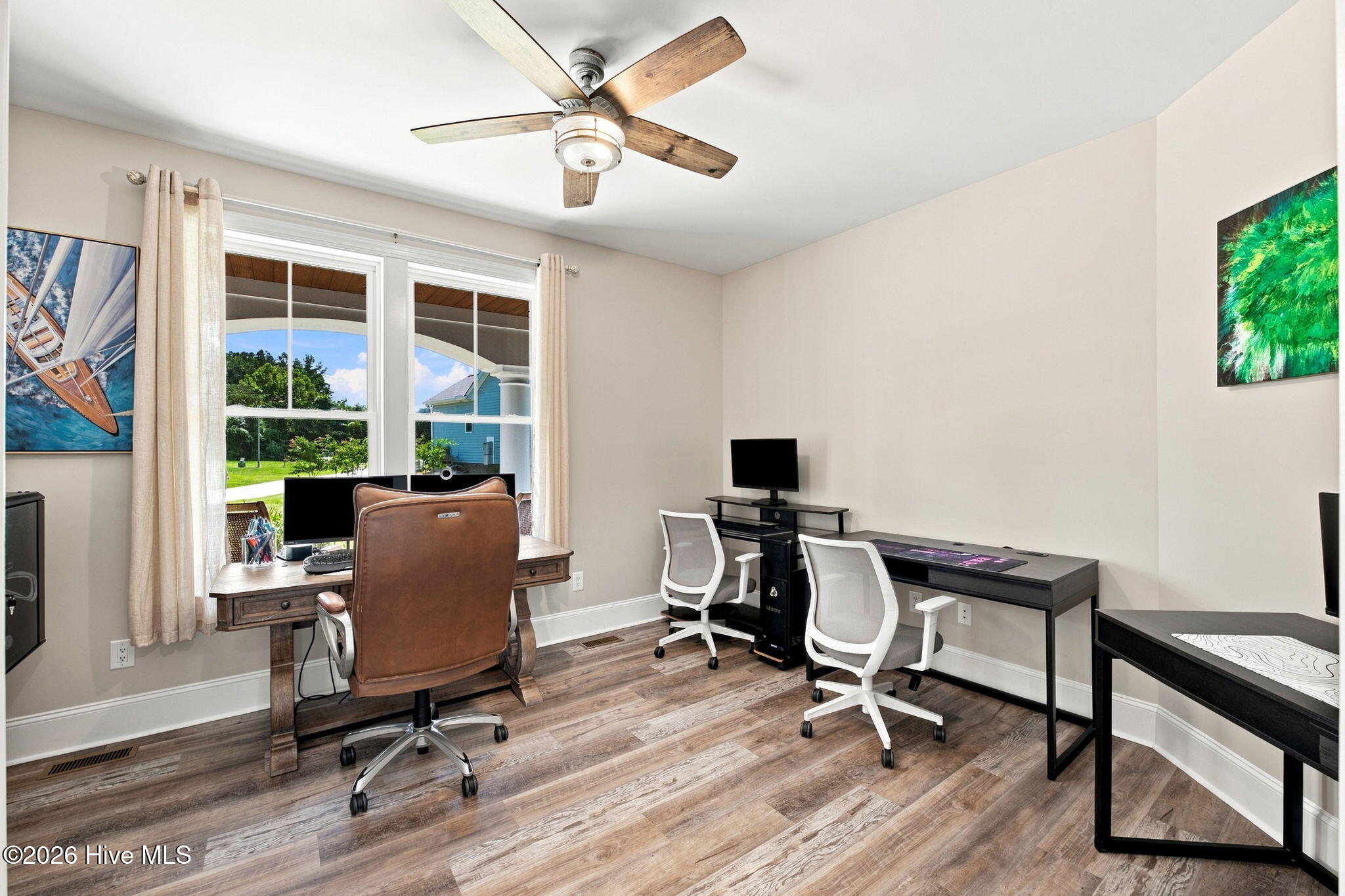 Furnished home office with two workstations, white chairs, and windows overlooking a green yard.