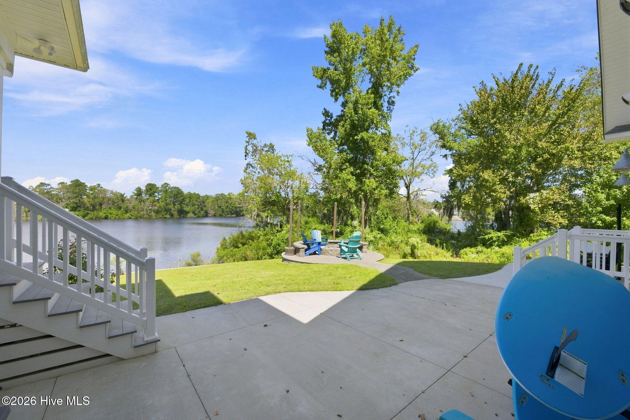 Waterfront backyard patio overlooking a lake, with Adirondack chairs and white deck stairs.