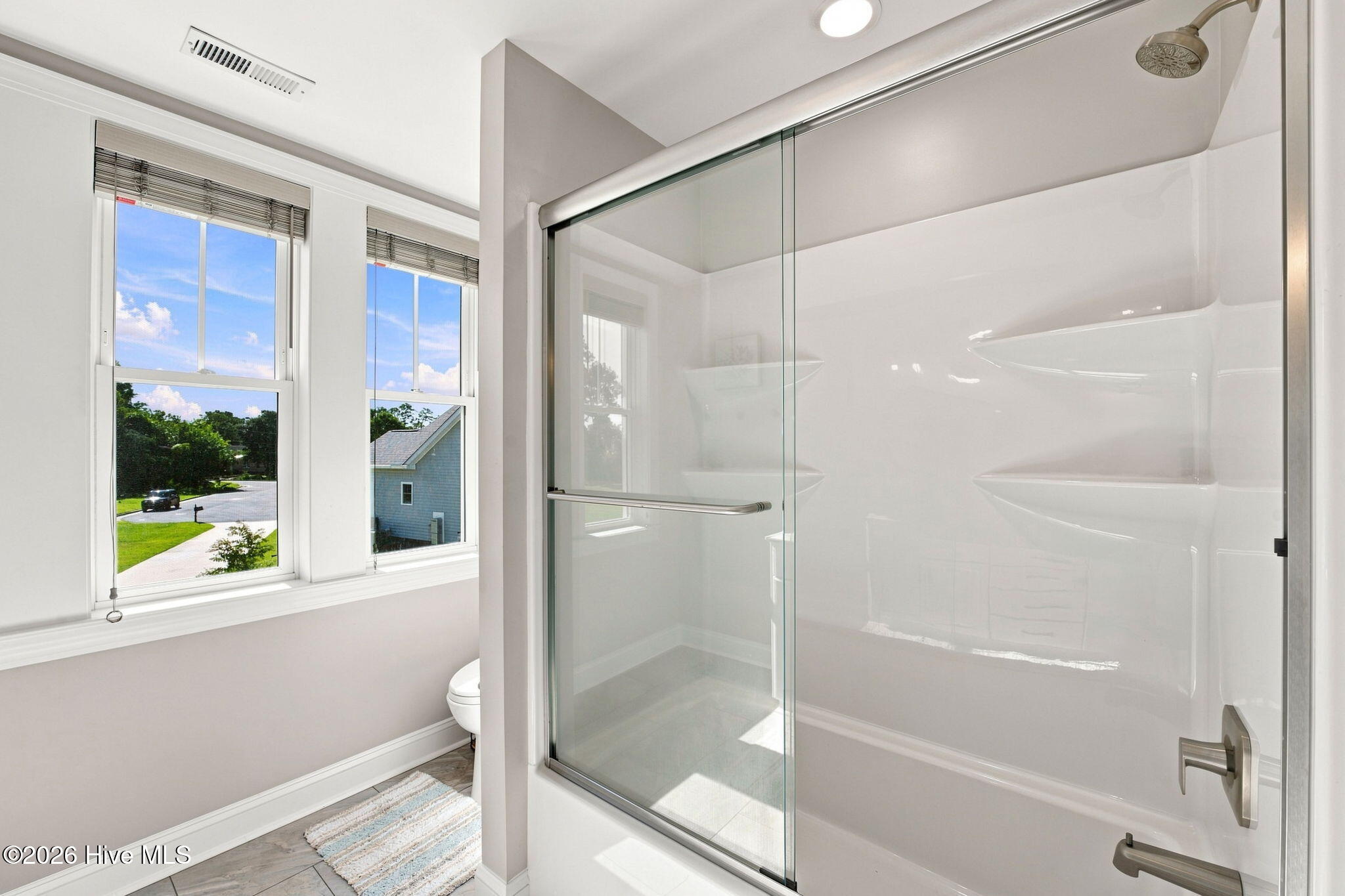 Bathroom with a glass-enclosed shower and two windows overlooking the street.
