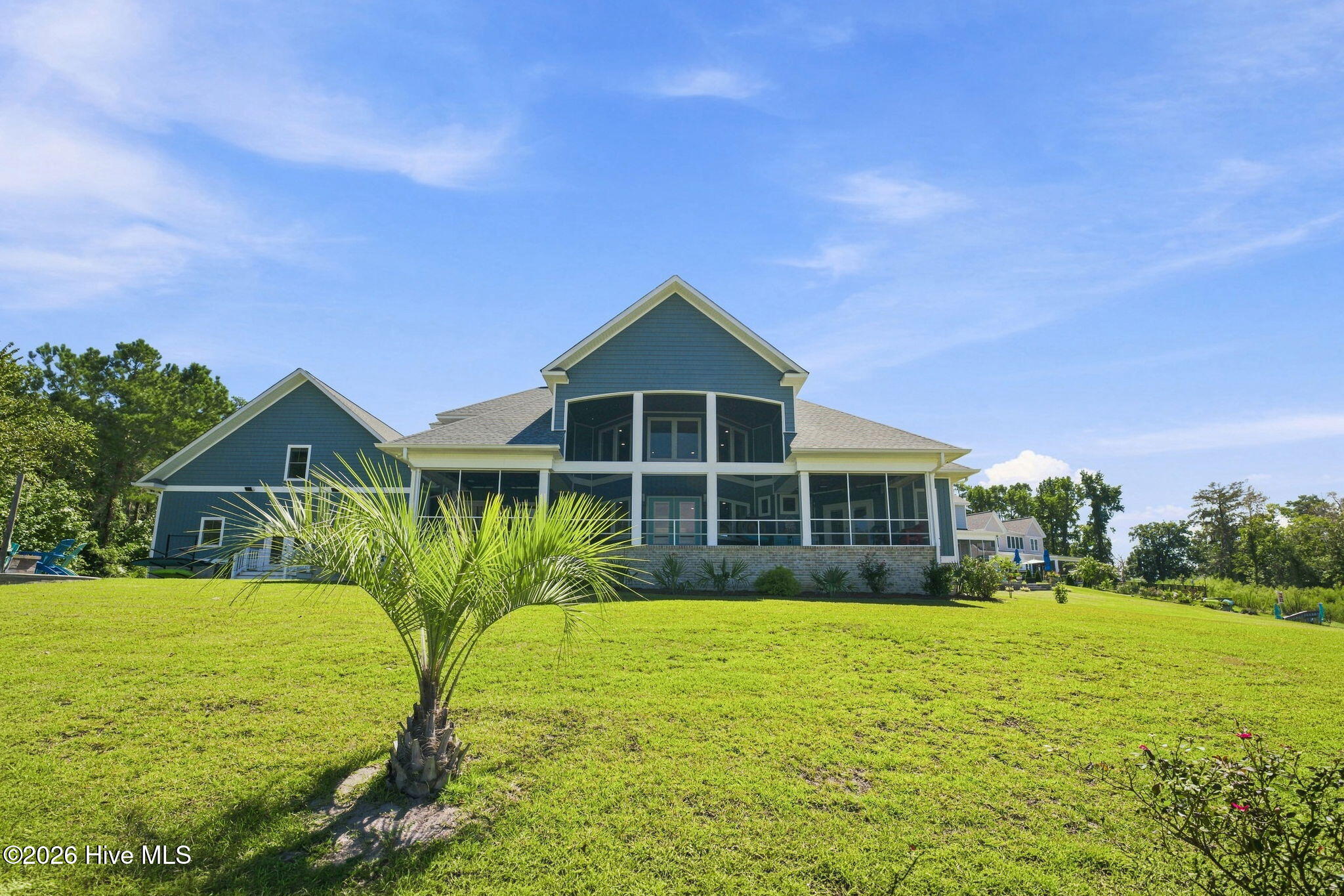 Blue-gray house with a two-story screened porch overlooking a broad lawn.
