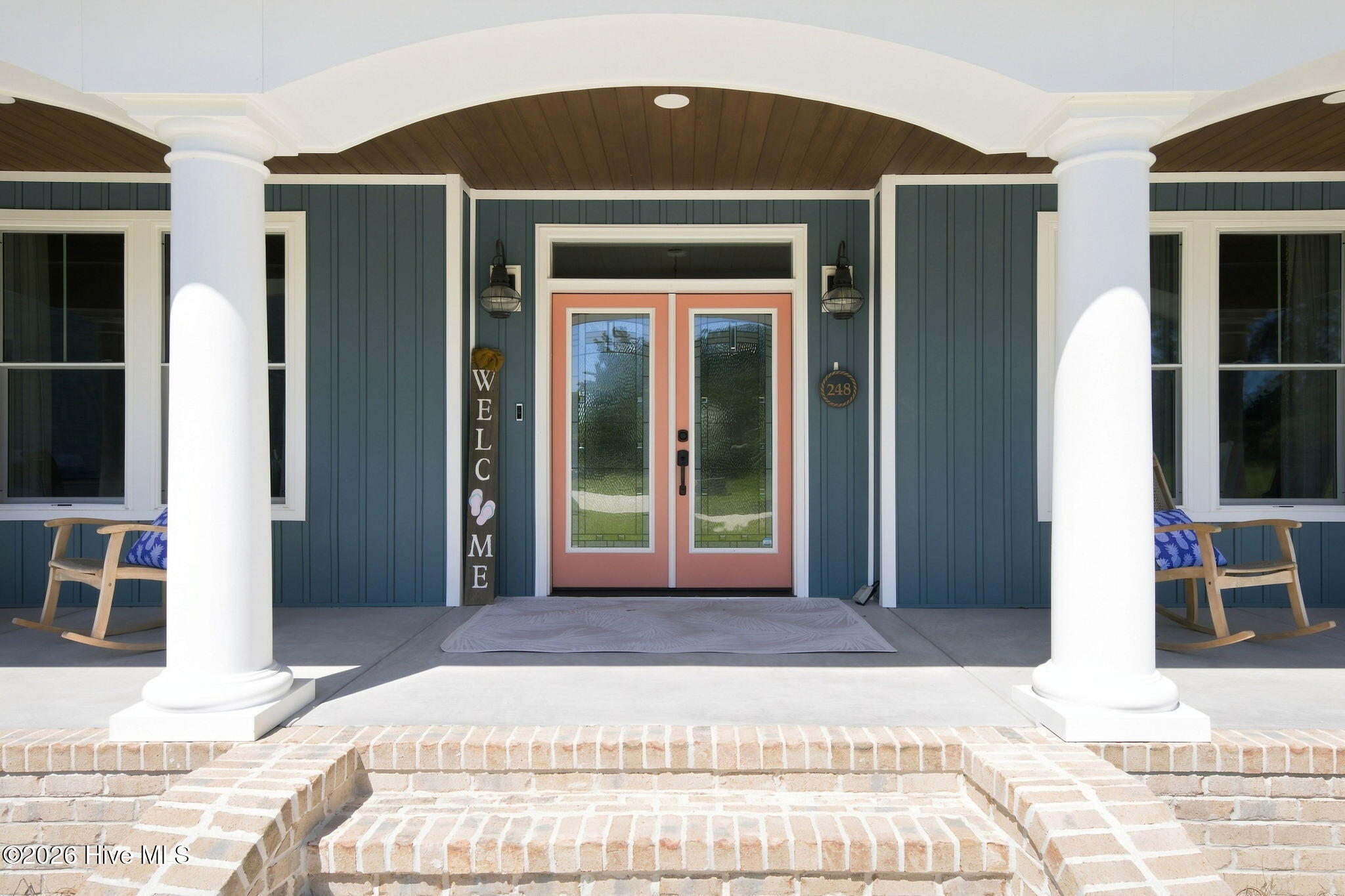 Front porch with coral double doors, white columns, brick steps, and wooden rocking chairs.