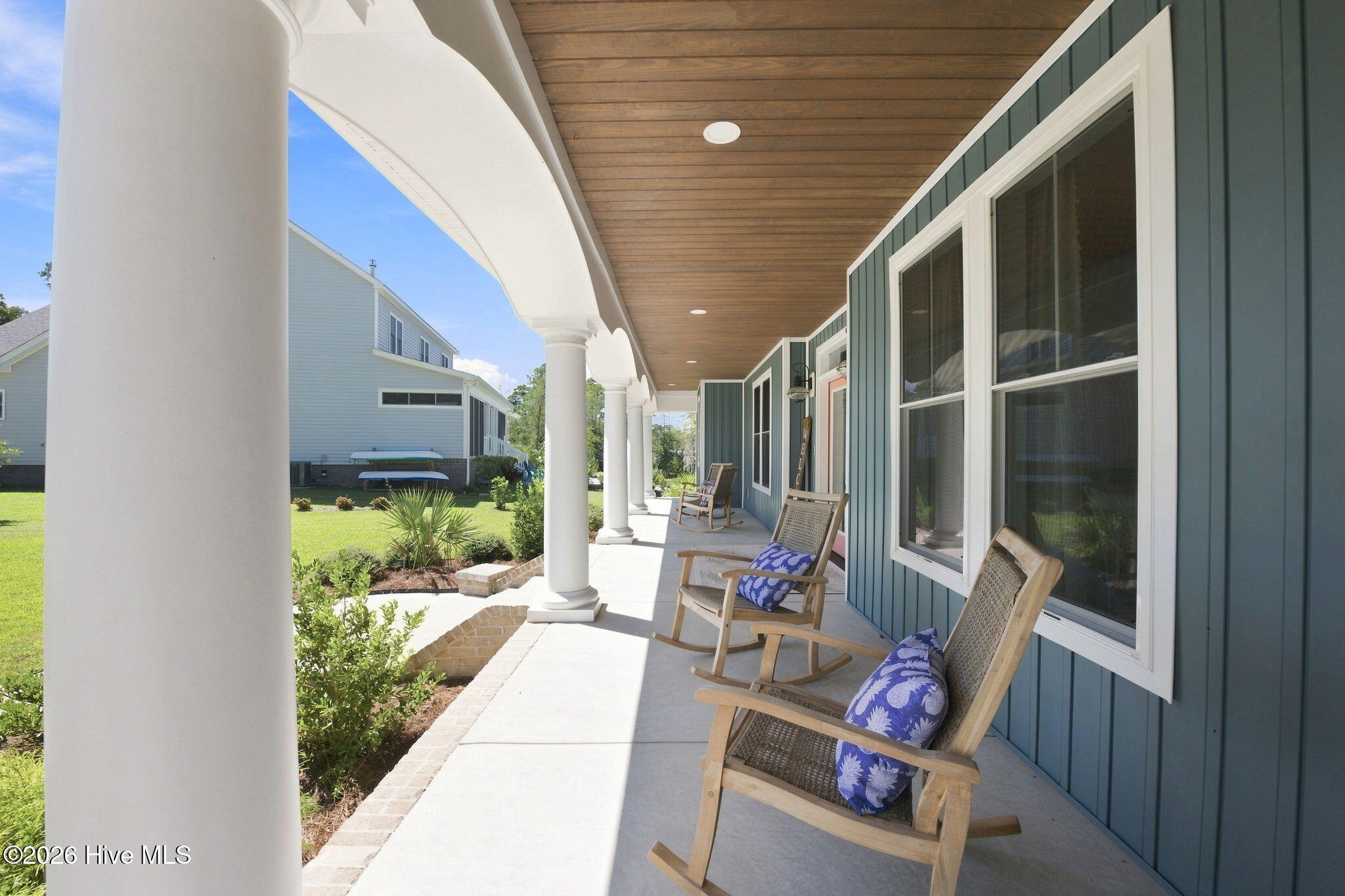 Covered porch with white columns, a wood ceiling, and rocking chairs beside blue siding.