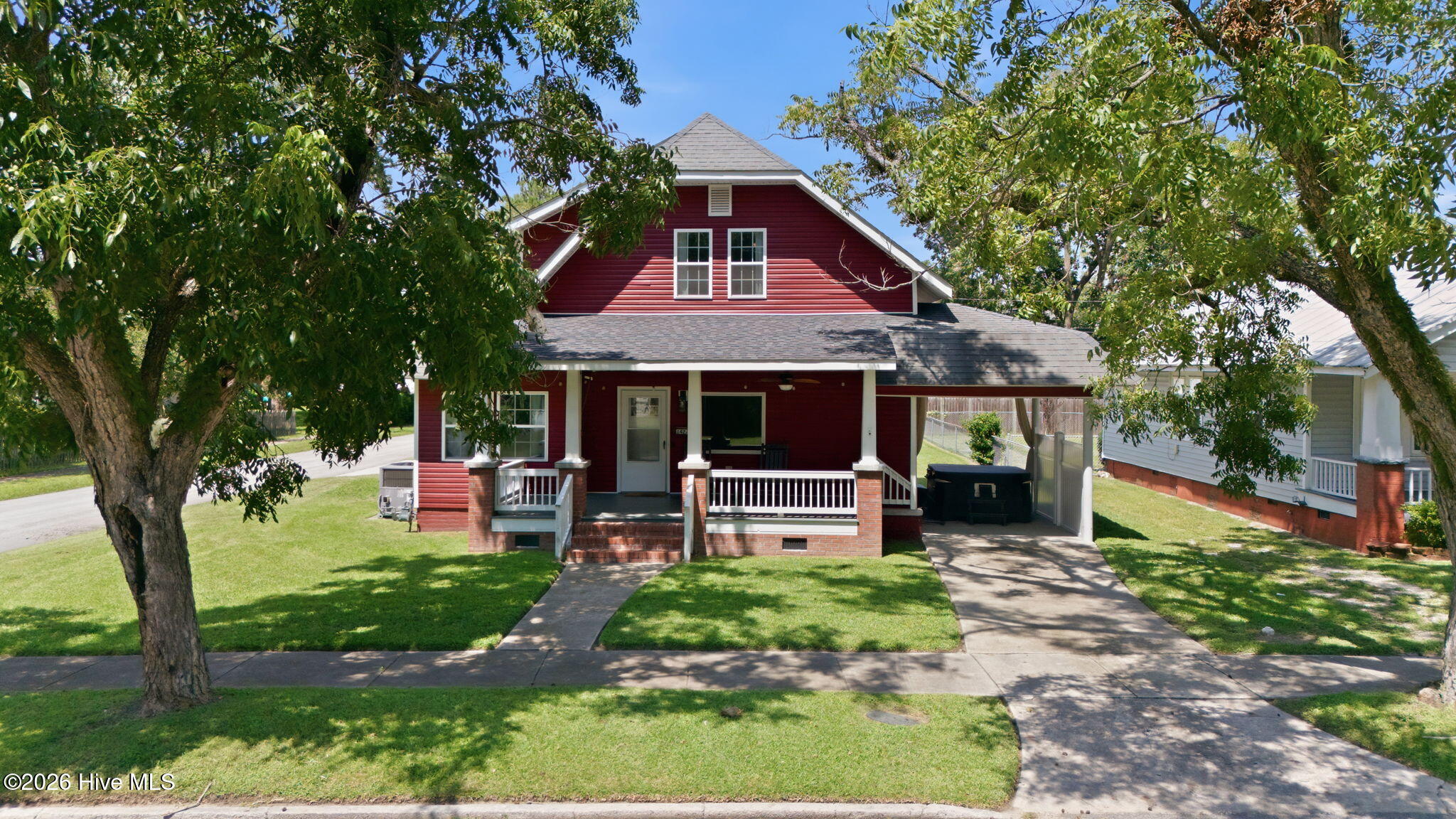 Red two-story house with a covered porch, brick steps, and mature shade trees.