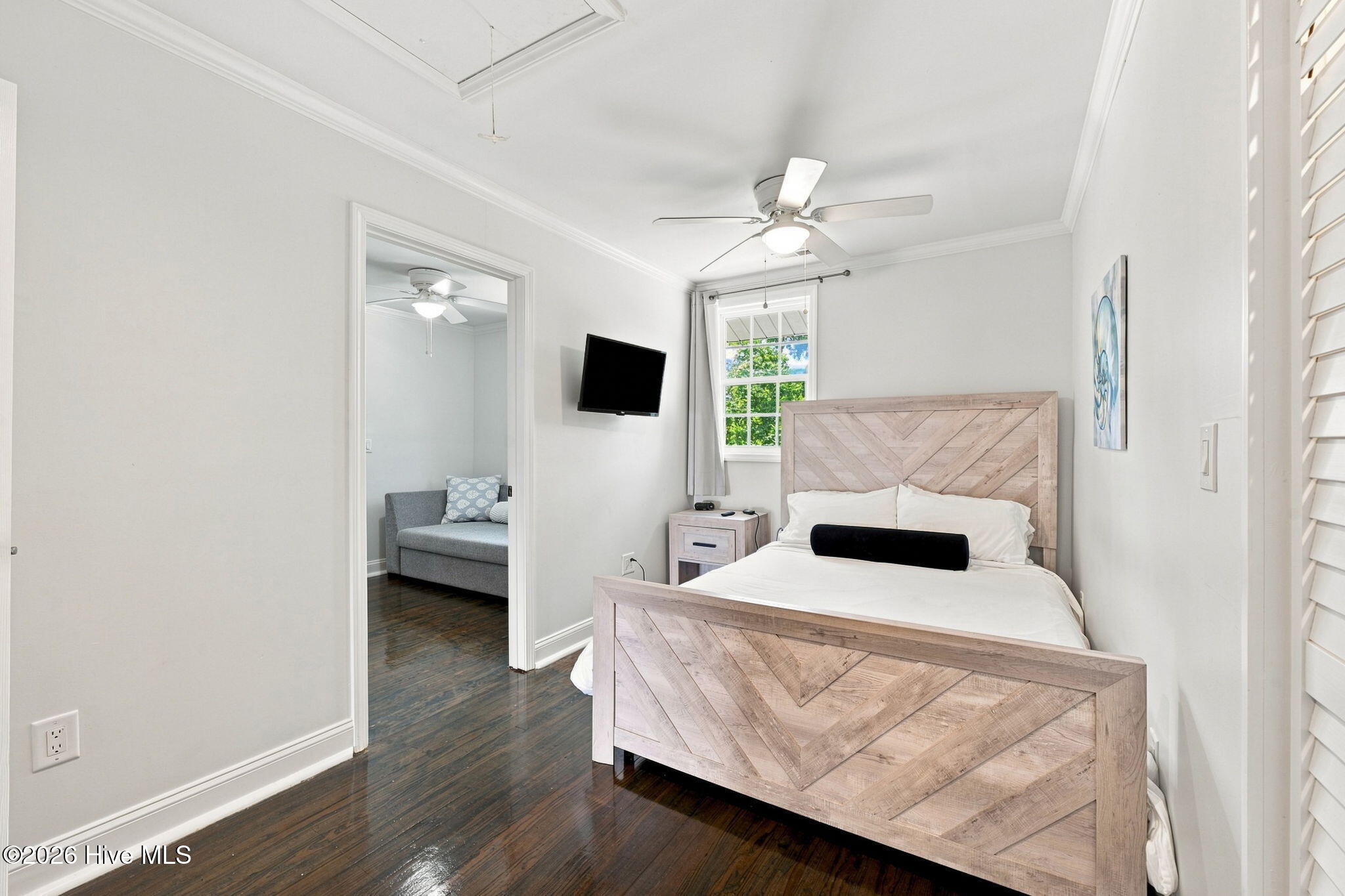 Bedroom with a pale geometric wood bed frame and an adjoining sitting area with a gray sofa.