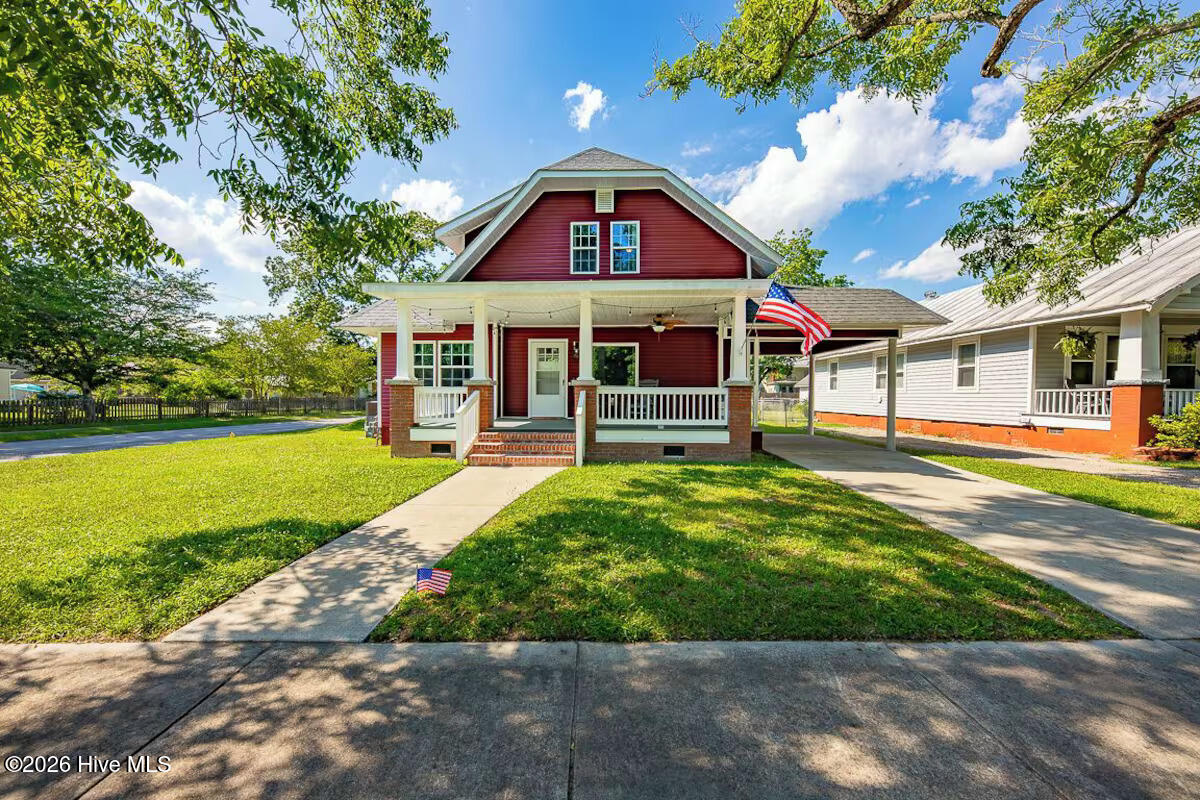 Red house with white-trimmed covered porch, American flag, and walkway through the front lawn.