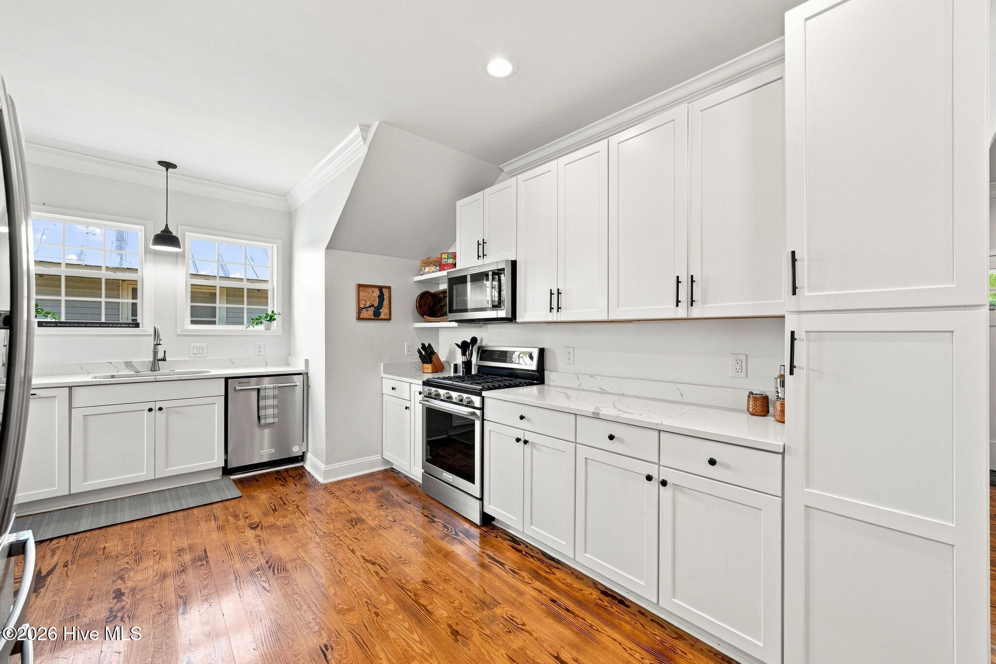 Bright kitchen with white cabinets, stainless steel appliances, and warm hardwood floors.