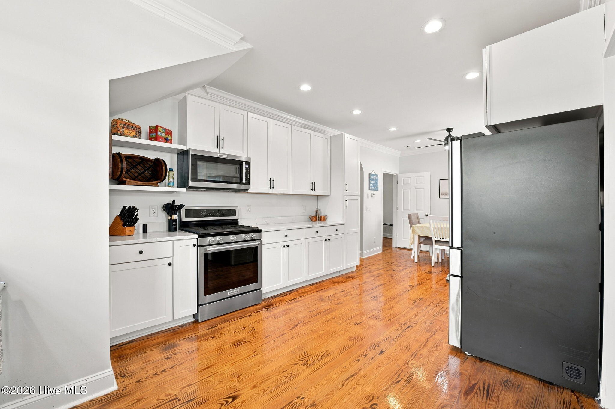 Kitchen with white cabinetry, stainless steel appliances, and polished hardwood floors opening to a dining area.