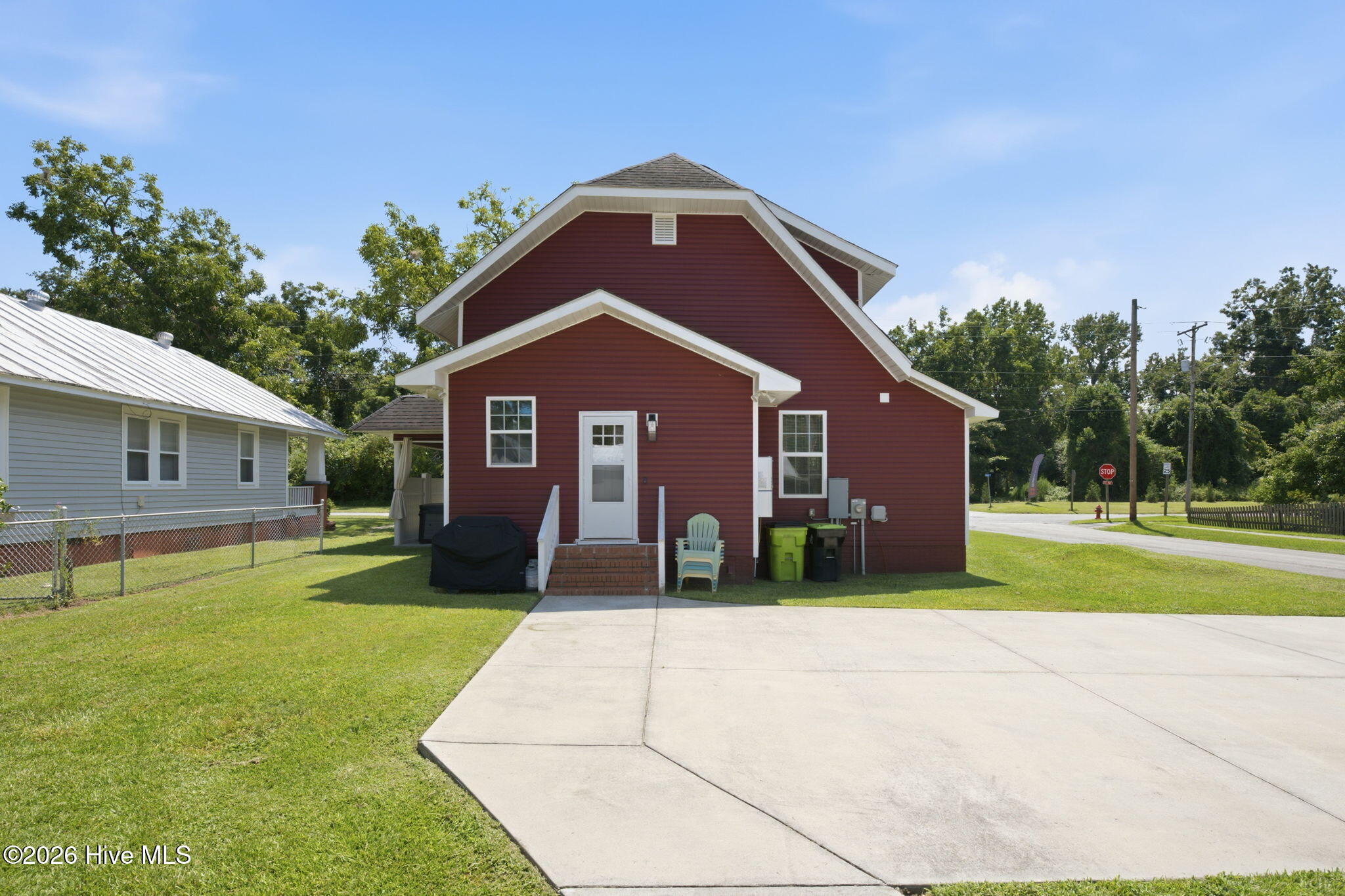 Red-sided house with white trim, entry steps, and a broad concrete driveway.