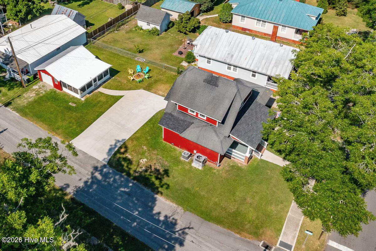 Aerial view of a red house with a dark roof, broad lawn, and concrete driveway.