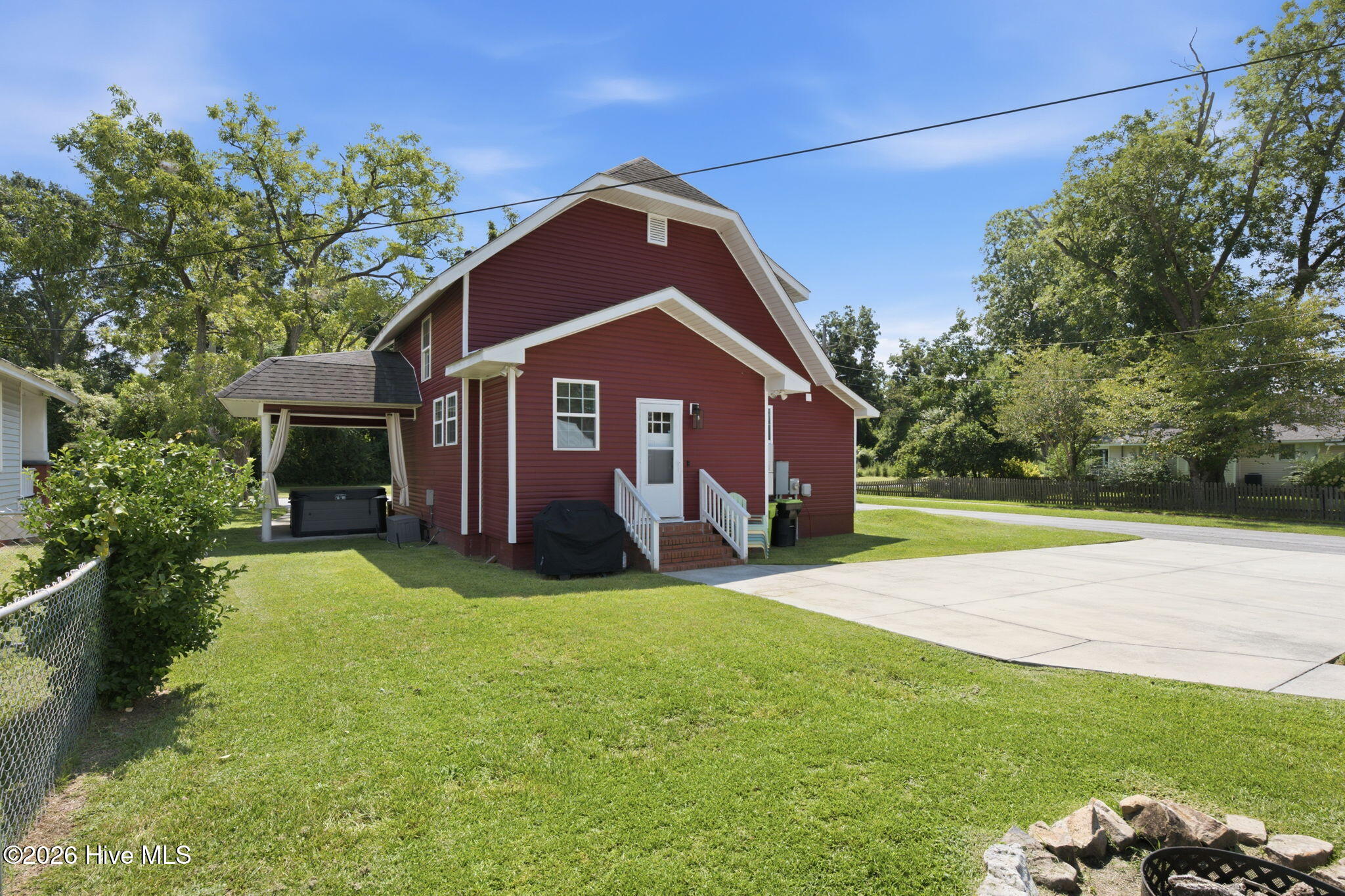 Red barn-style house with white trim, covered patio, brick steps, and a wide concrete driveway.