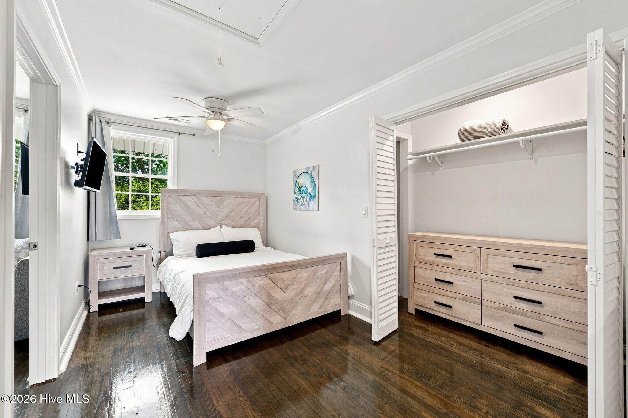 Bedroom with pale wood furniture, dark hardwood floors, and an open louvered closet.