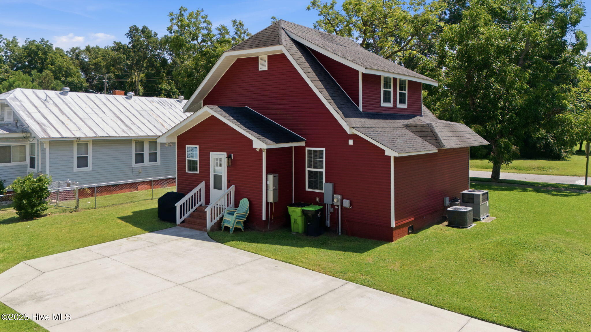 Red two-story home with white trim, steep gabled roof, lawn, and broad concrete driveway.