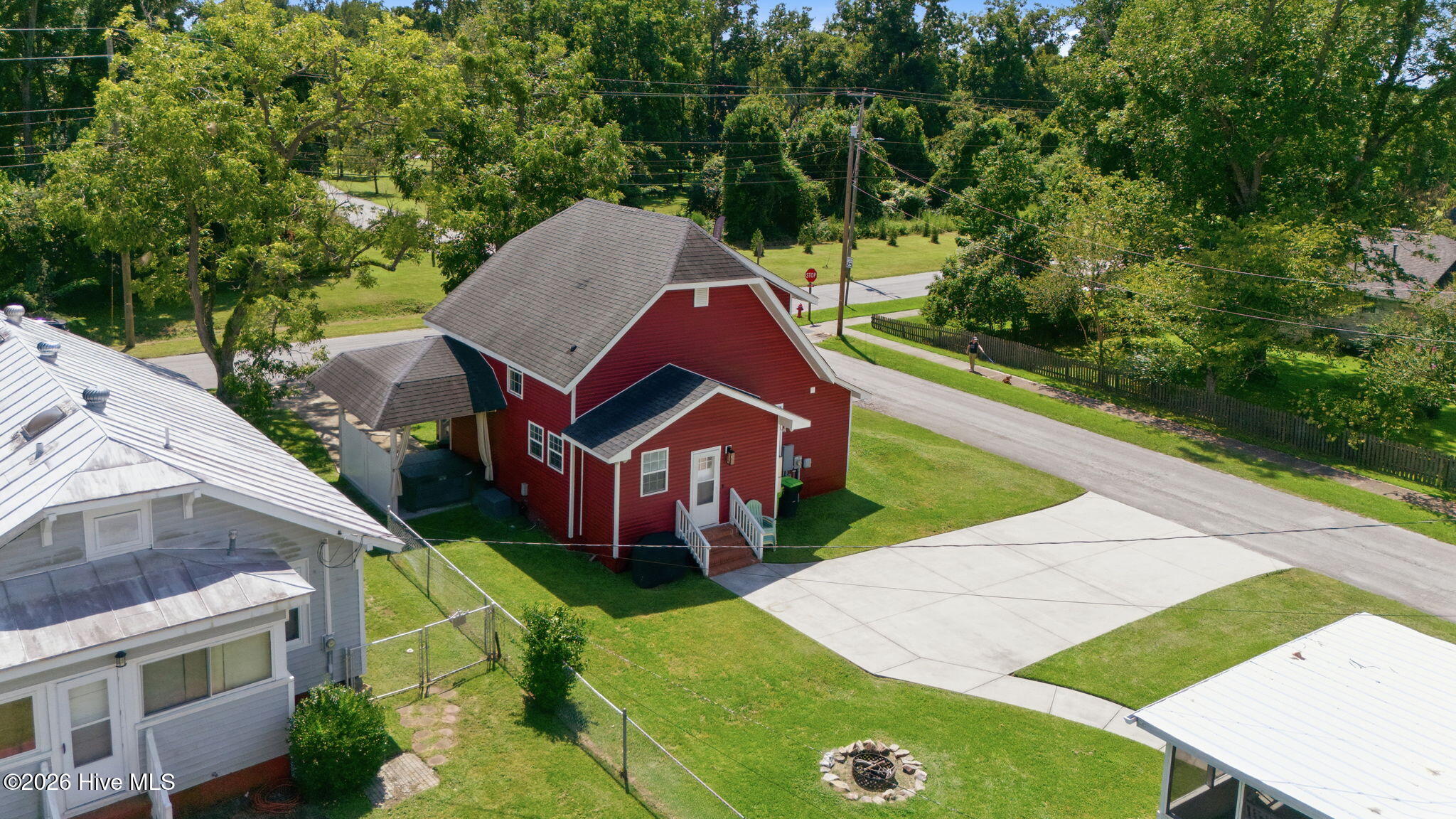 Aerial view of a red-sided property with a gray roof, broad driveway, and tree-lined yard.