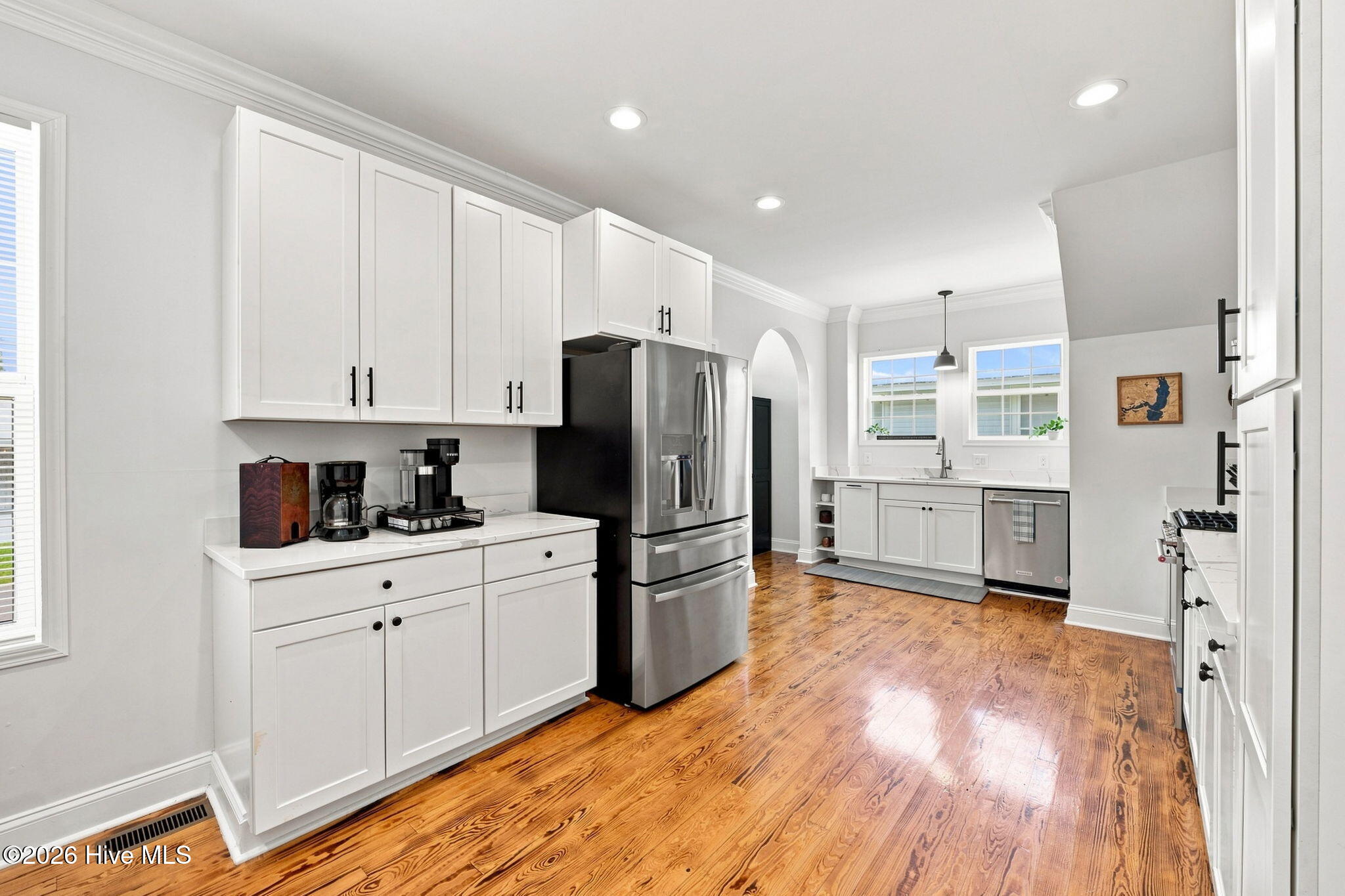 Kitchen with white cabinetry, stainless steel appliances, and warm hardwood floors.