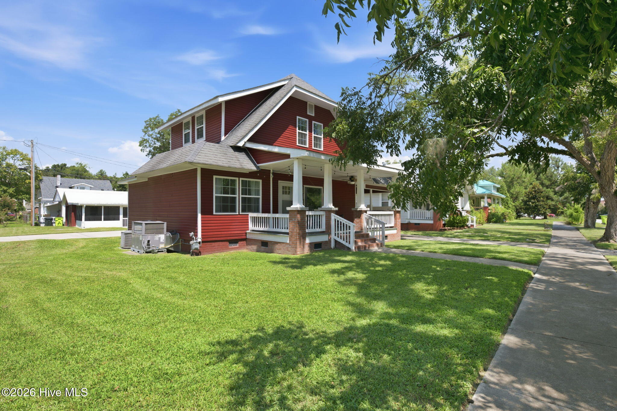 Two-story red house with a covered porch, brick supports, and a large shaded lawn.