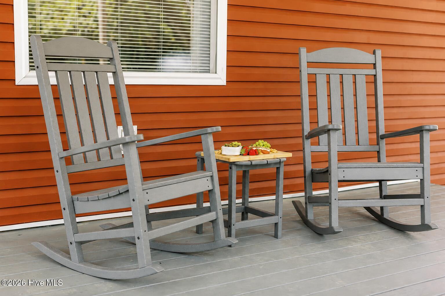 Gray rocking chairs and a snack table on a deck against orange siding.
