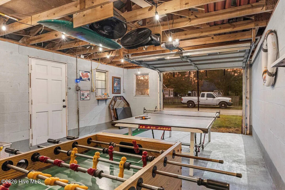 Garage game room with foosball and ping-pong tables beneath exposed ceiling joists.