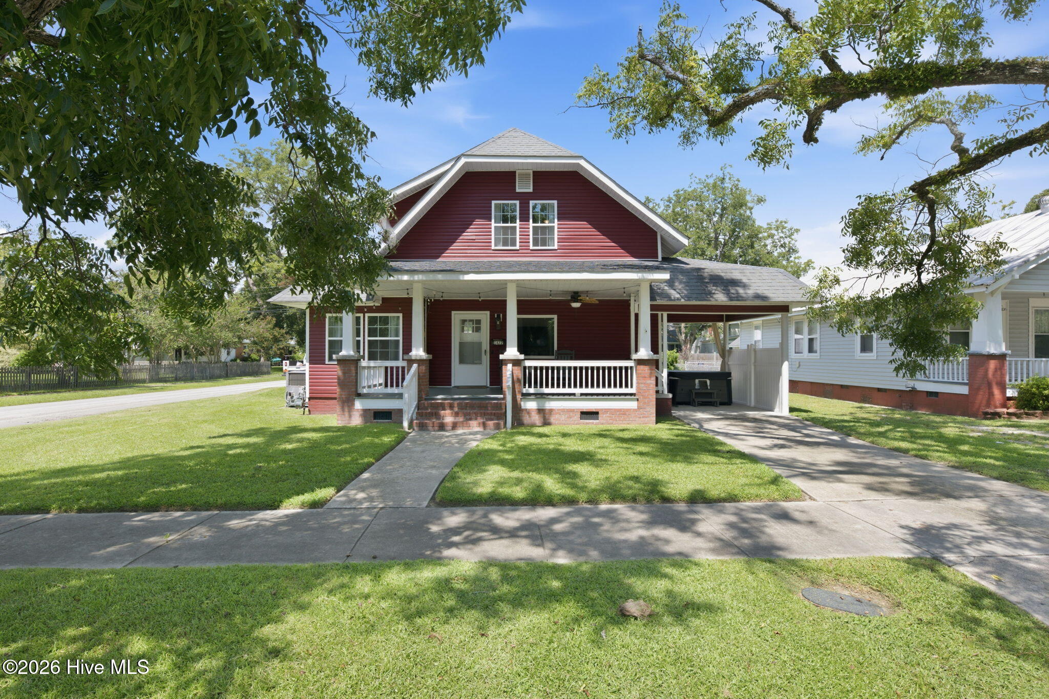 Red-sided house with a covered front porch and attached carport, framed by mature trees.