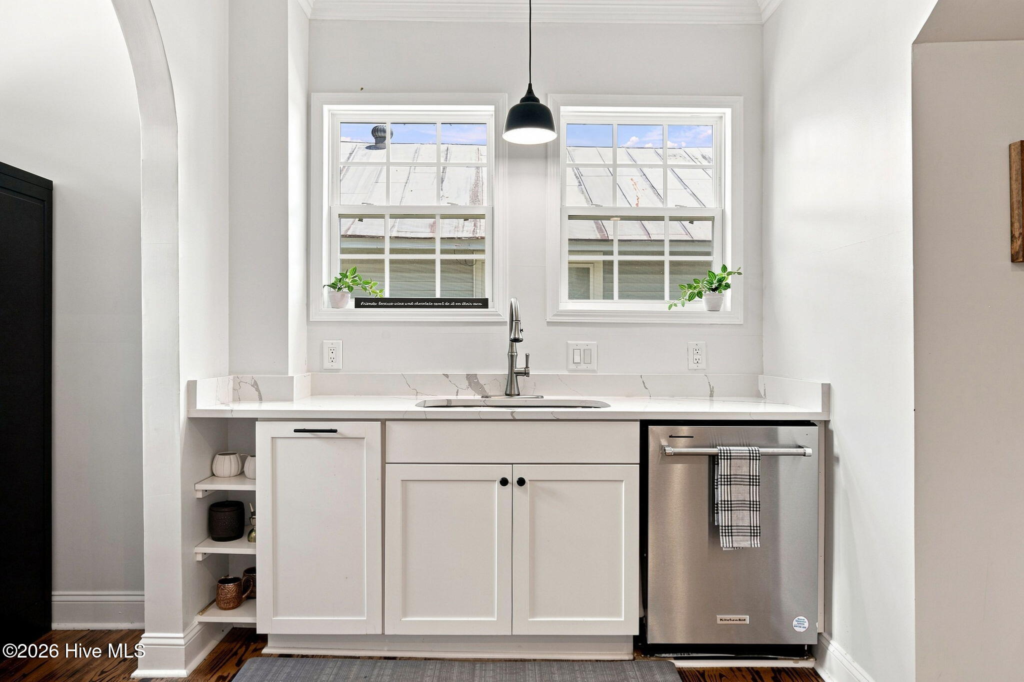 Bright kitchen with white cabinetry, marble-look counters, two windows, and a stainless-steel dishwasher.