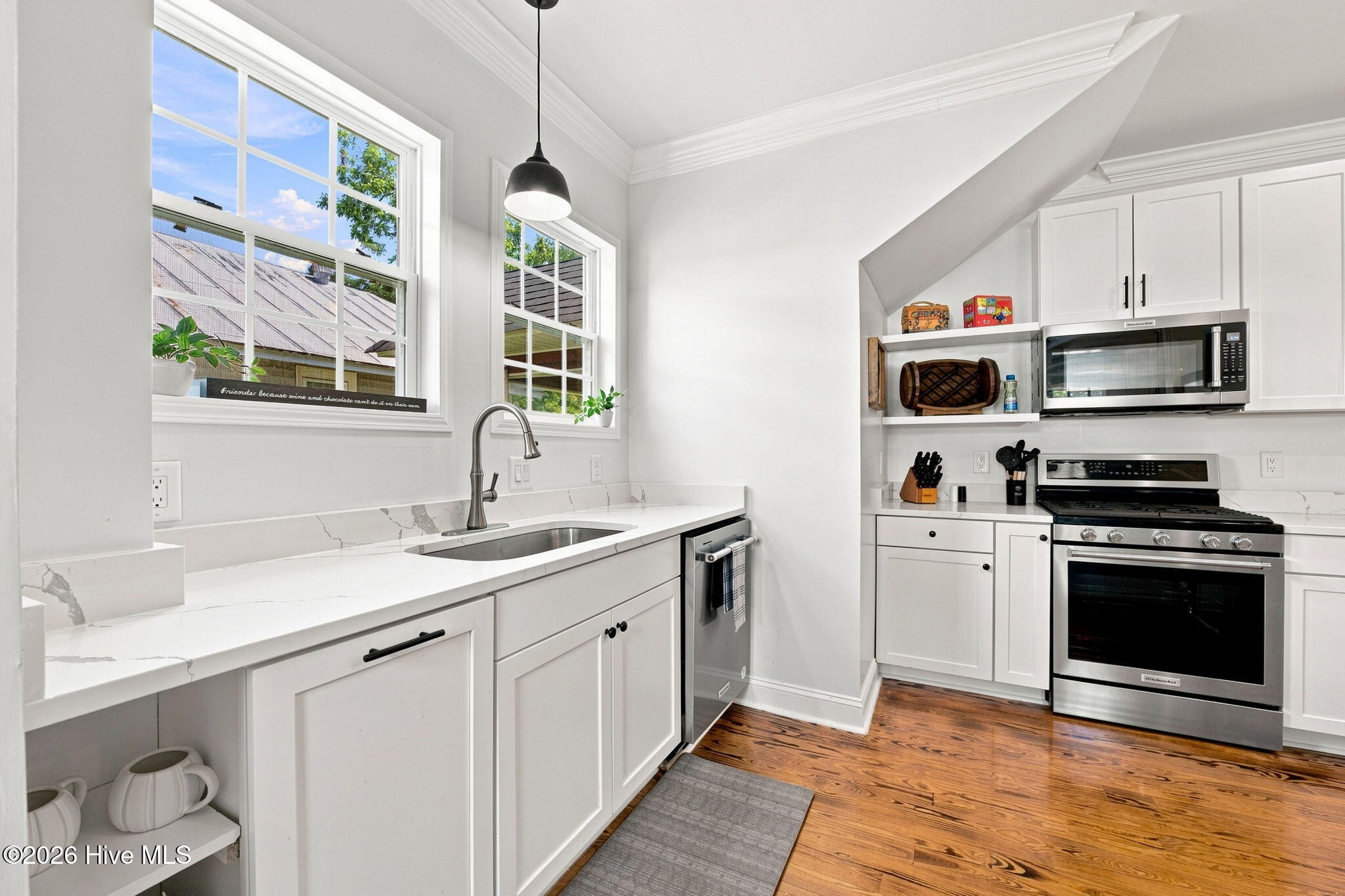 Bright white kitchen with stainless appliances, veined countertops, and large windows over the sink.