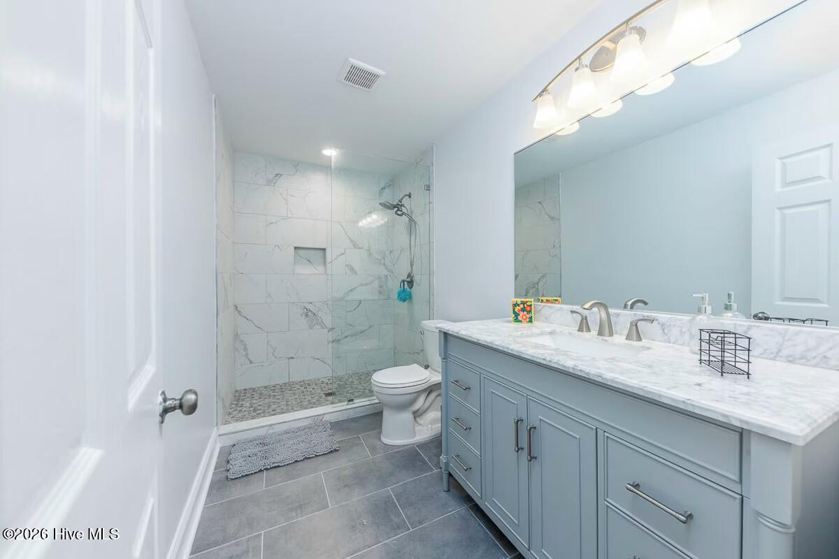 Bathroom with a marble-look walk-in shower and blue-gray double vanity.
