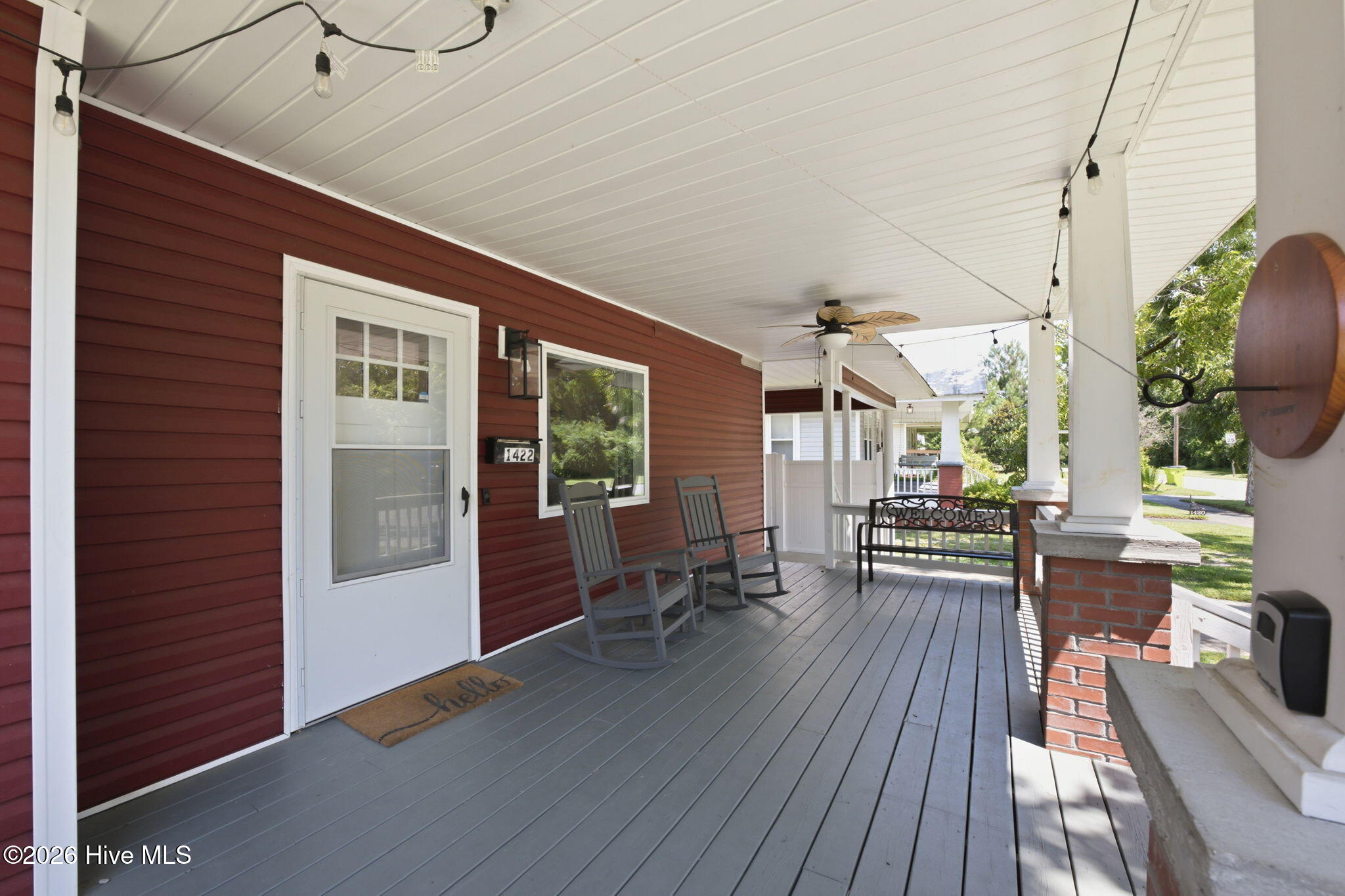 Covered front porch with gray decking, white columns, rocking chairs, and red siding.