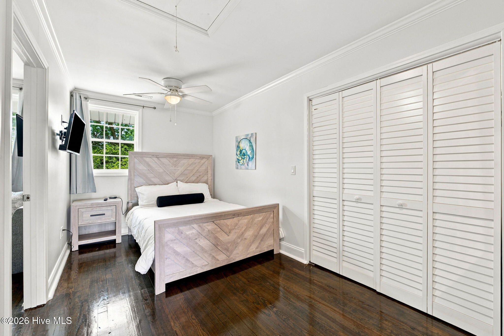 Bedroom with a light wood bed, dark hardwood floors, and white louvered closet doors.