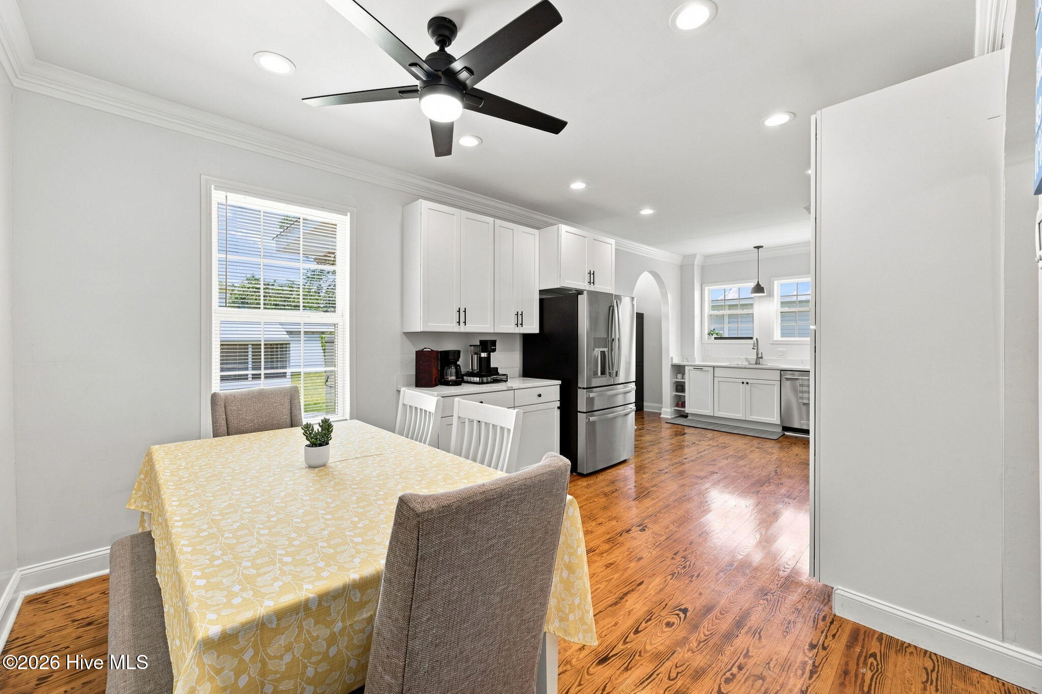 Furnished kitchen and dining area with white cabinets, stainless steel appliances, hardwood floors, and a yellow tablecloth.