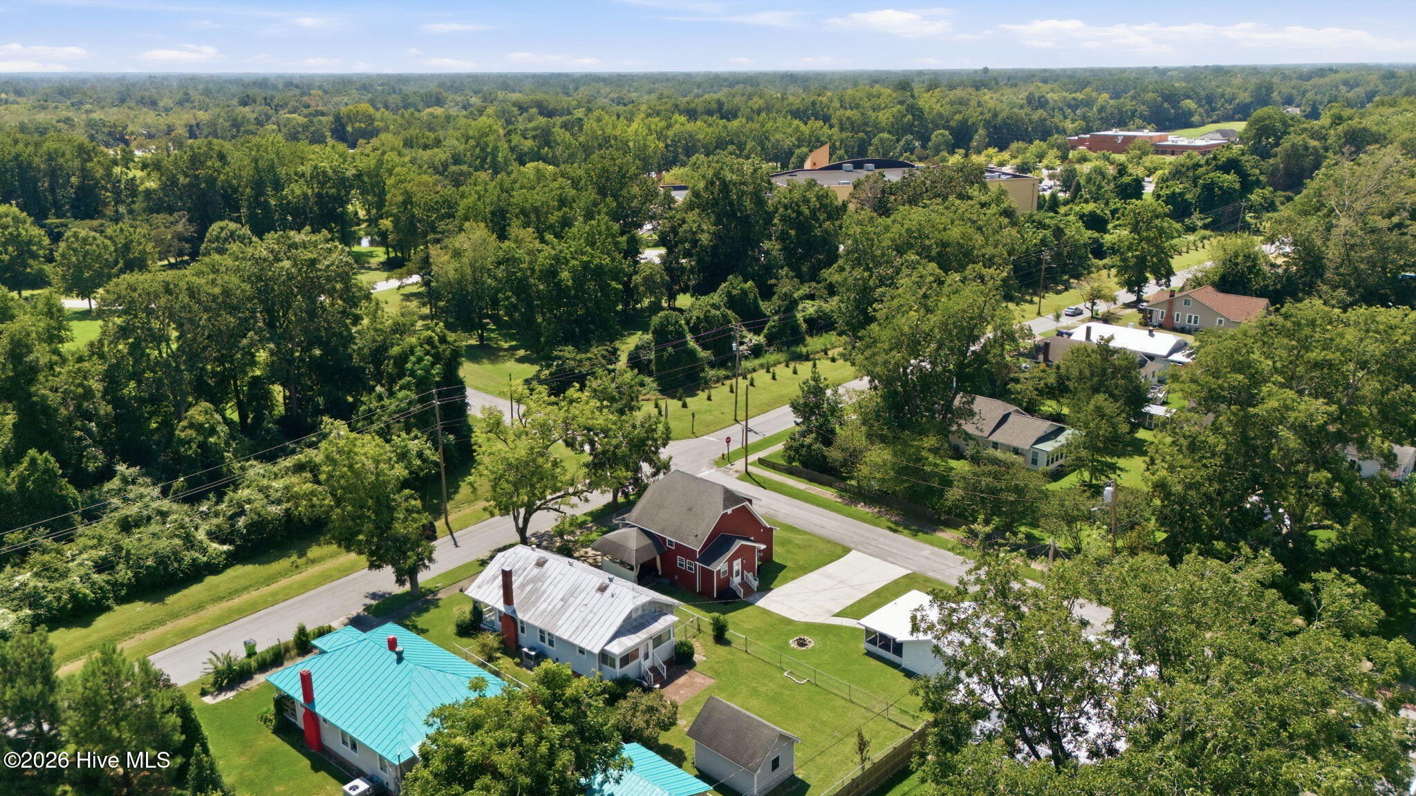 Aerial view of a leafy neighborhood with a red-sided home in the foreground and a large building beyond.
