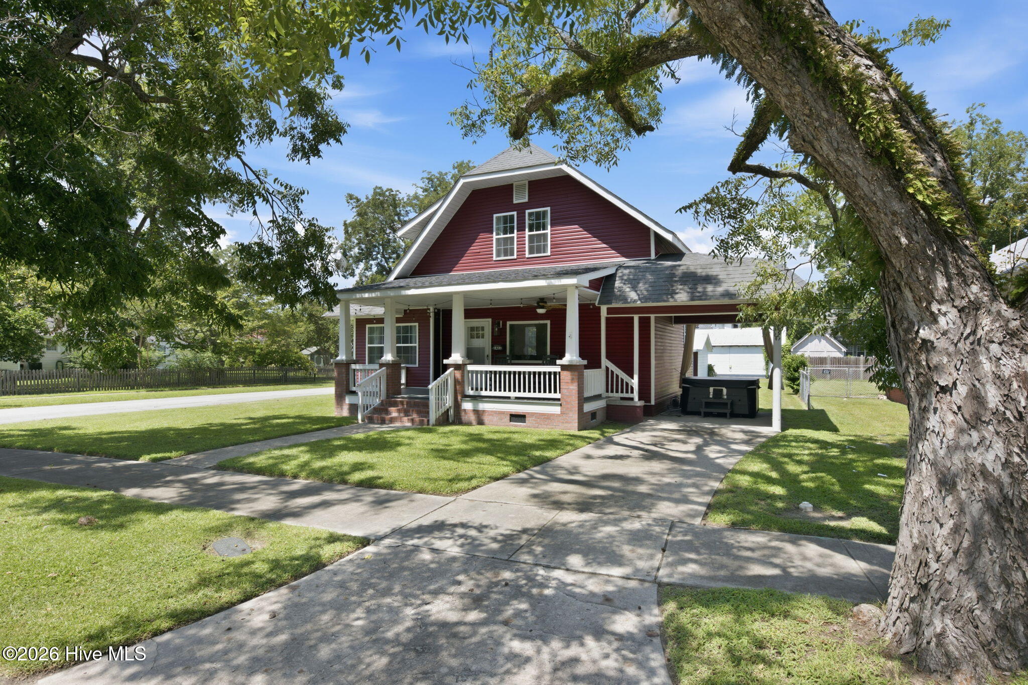 Red two-story house with a covered porch and carport beneath mature shade trees.