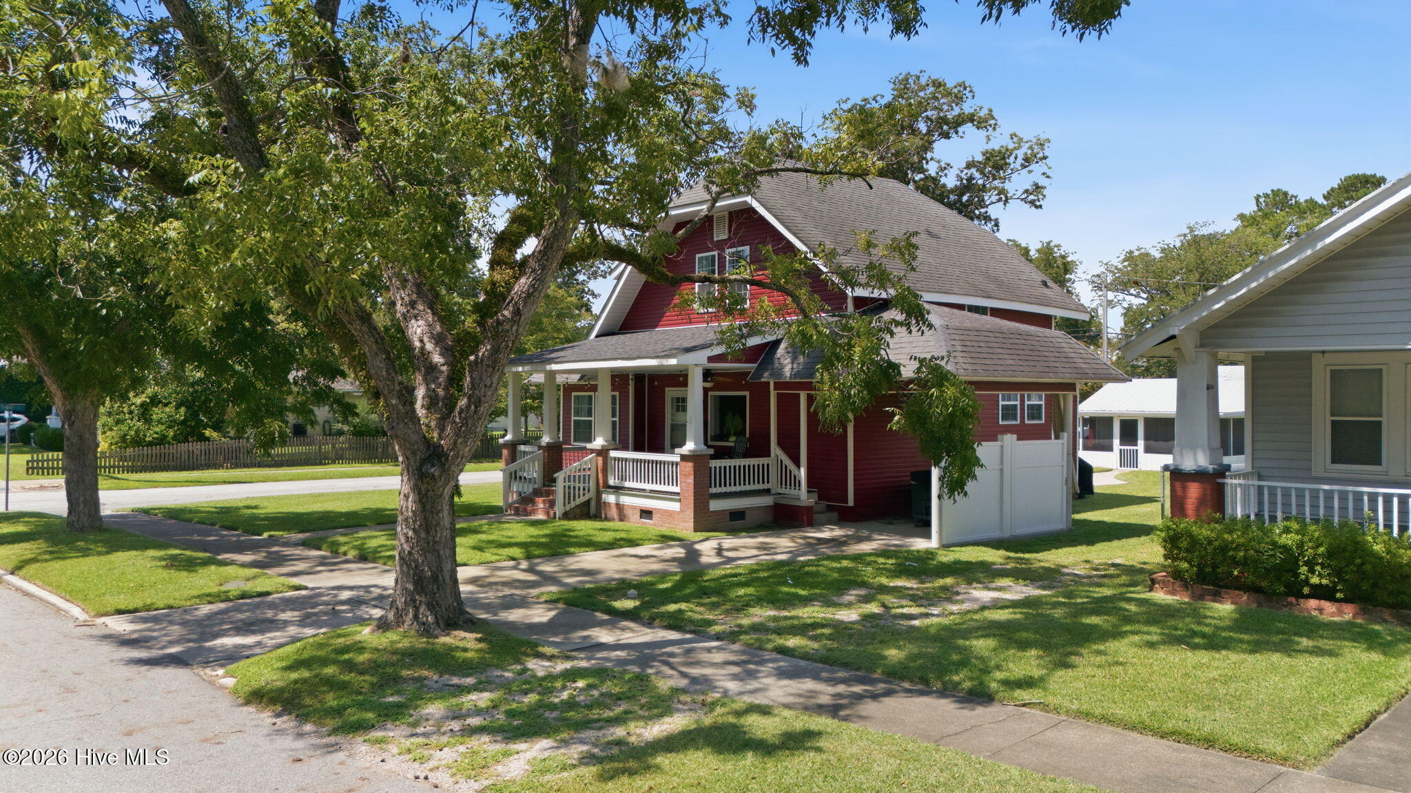 Red two-story house with a broad gray roof and covered porch, partly screened by mature trees.