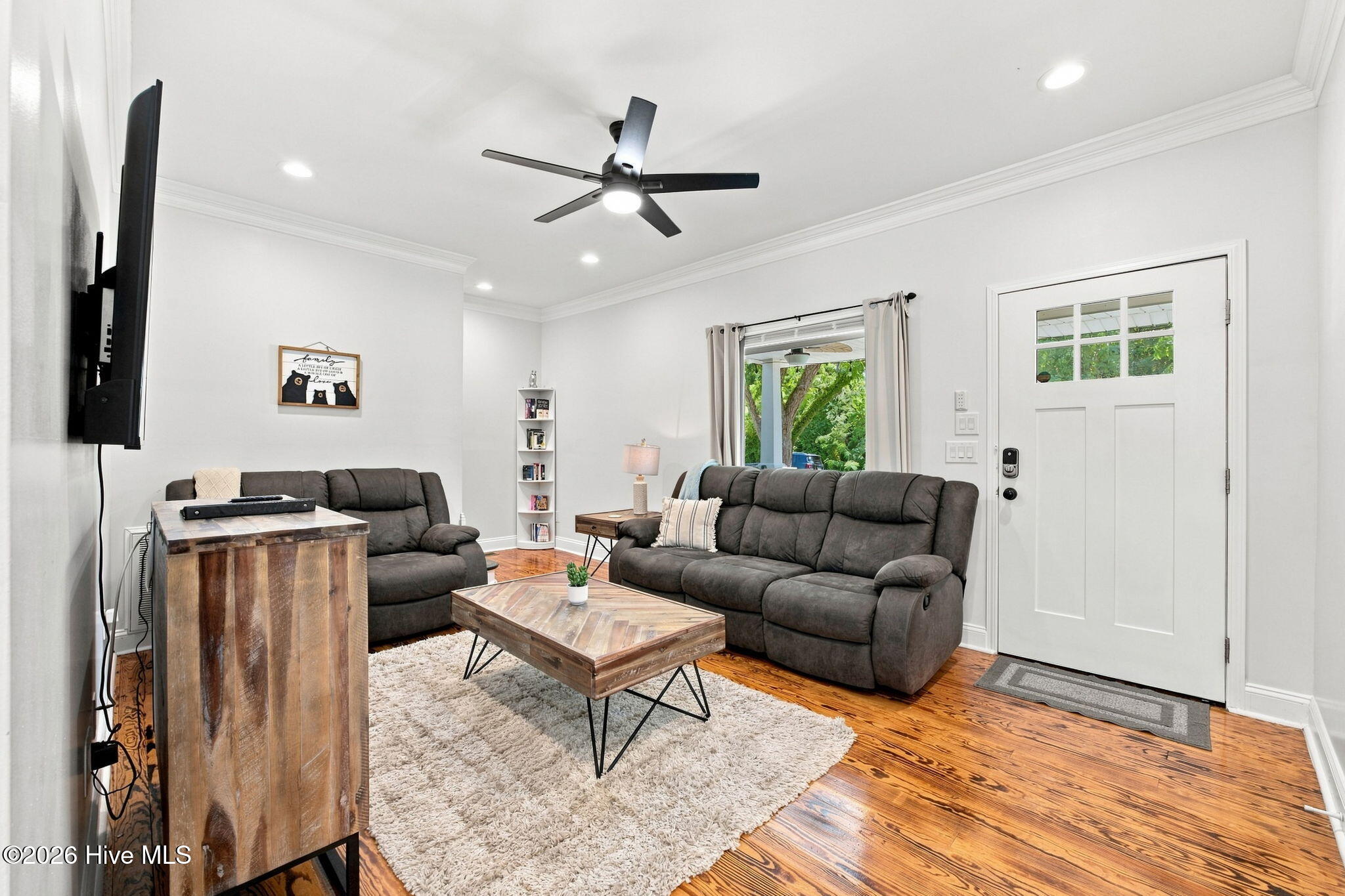 Living room with gray reclining sofas, rustic wood tables, hardwood floors, and a window overlooking greenery.