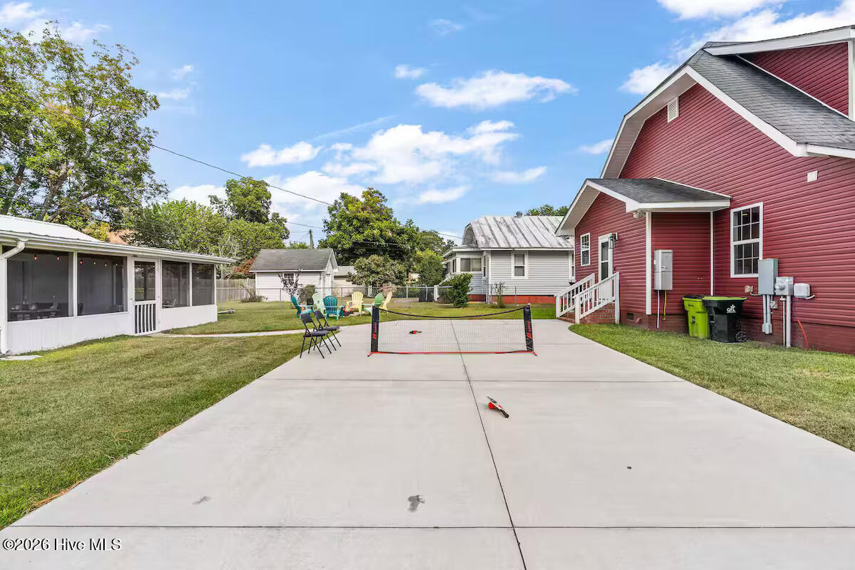 Backyard patio with a portable net beside a red-sided house and screened porch.