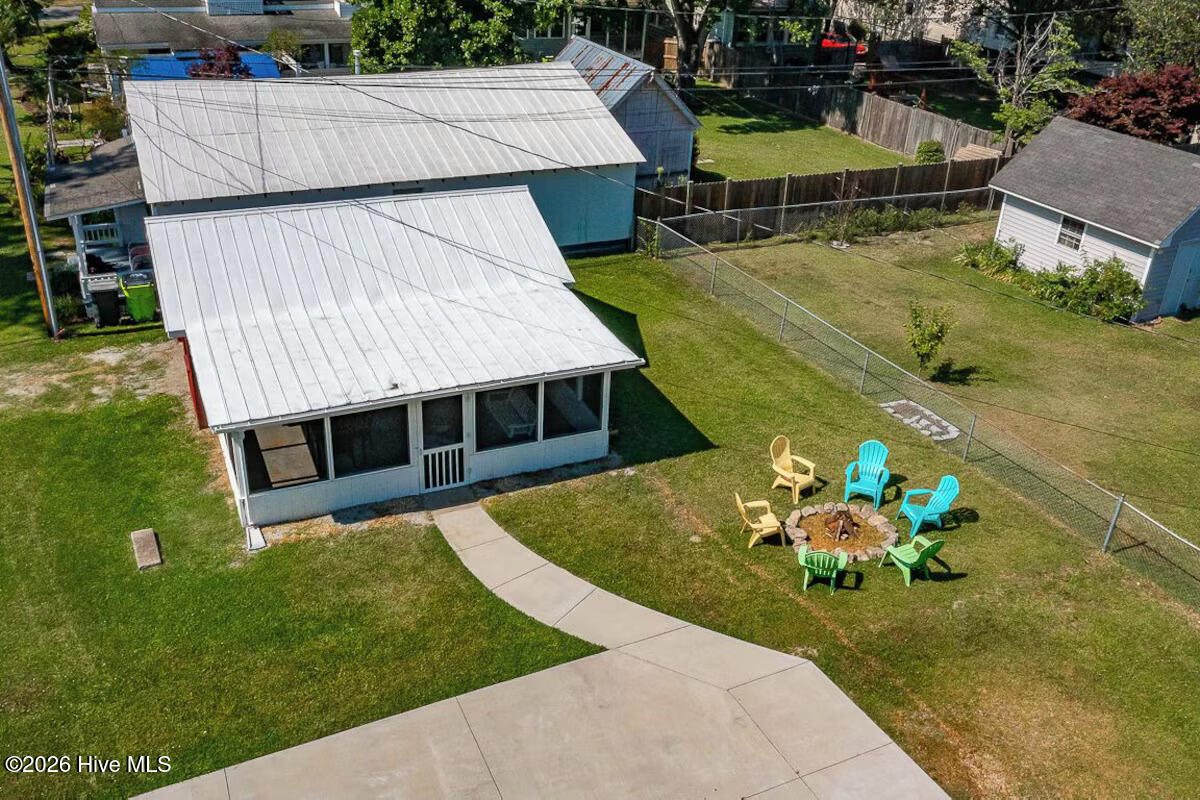 Aerial view of a blue home with metal roofs, fenced lawn, and fire pit seating.