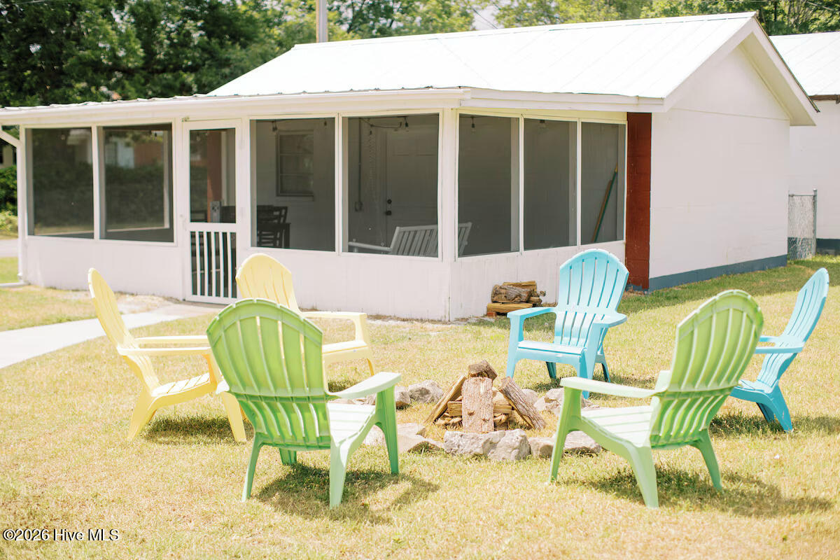 House exterior with a screened porch and colorful Adirondack chairs around a stone fire pit.