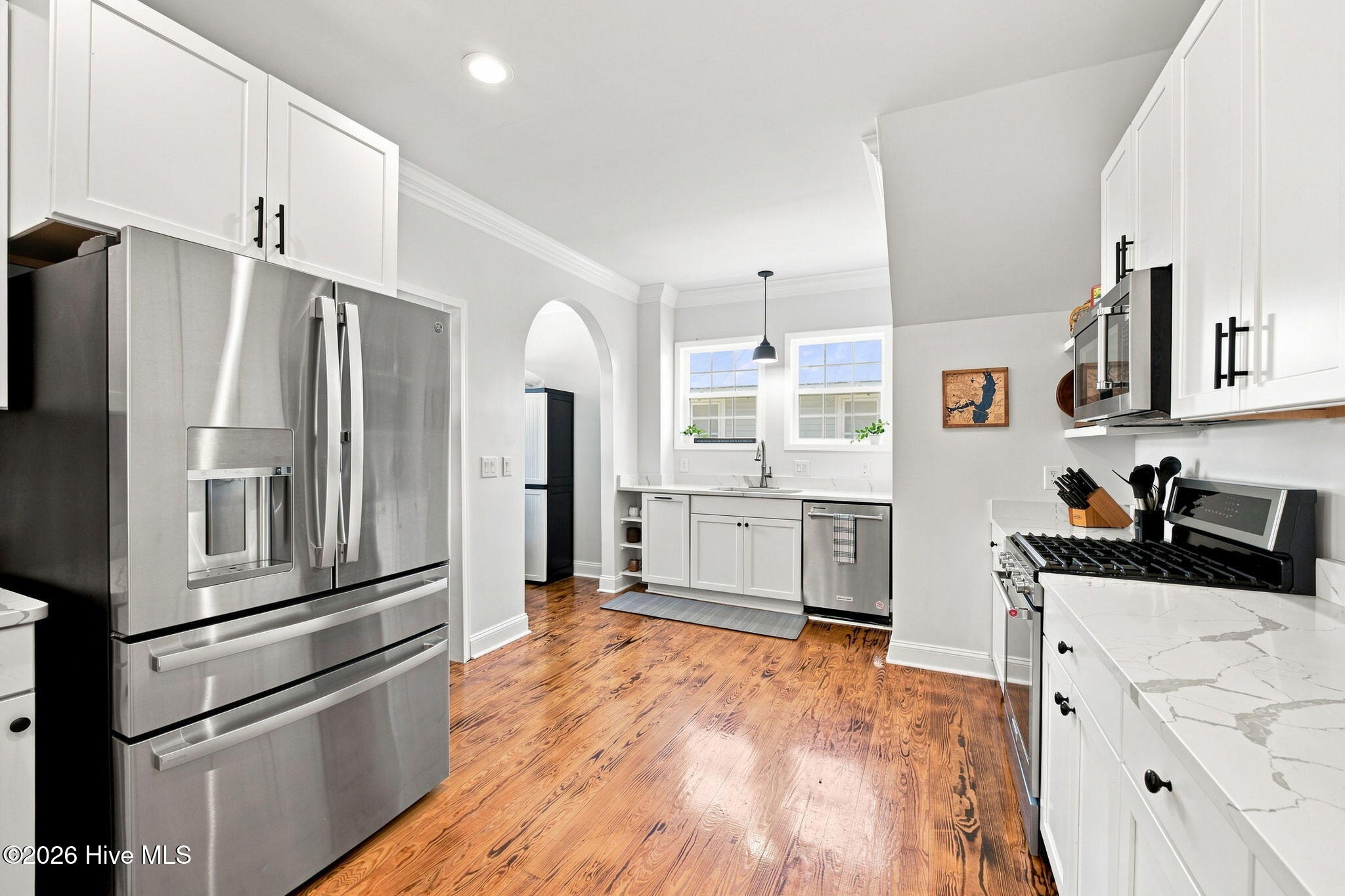 Kitchen with white cabinets, stainless appliances, veined countertops, and hardwood floors.
