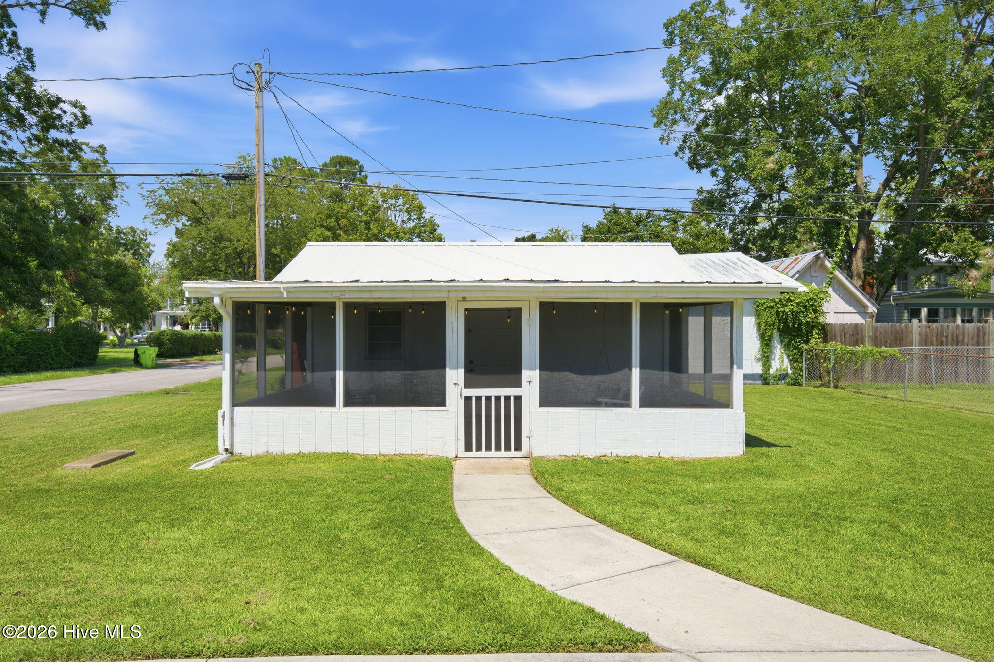 White single-story house with a wide screened porch, metal roof, and curved walkway across the lawn.