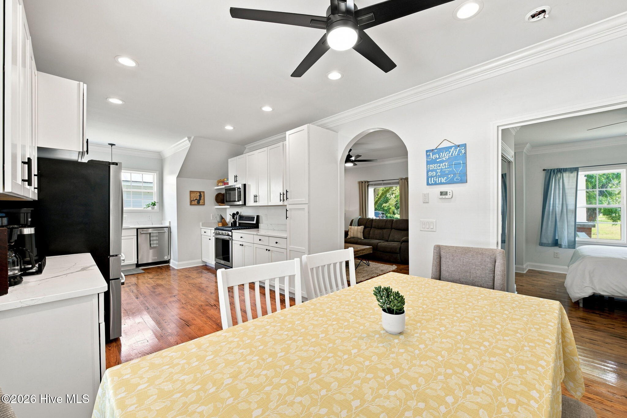Kitchen and dining area with white cabinets, hardwood floors, and an arched opening to the living room.