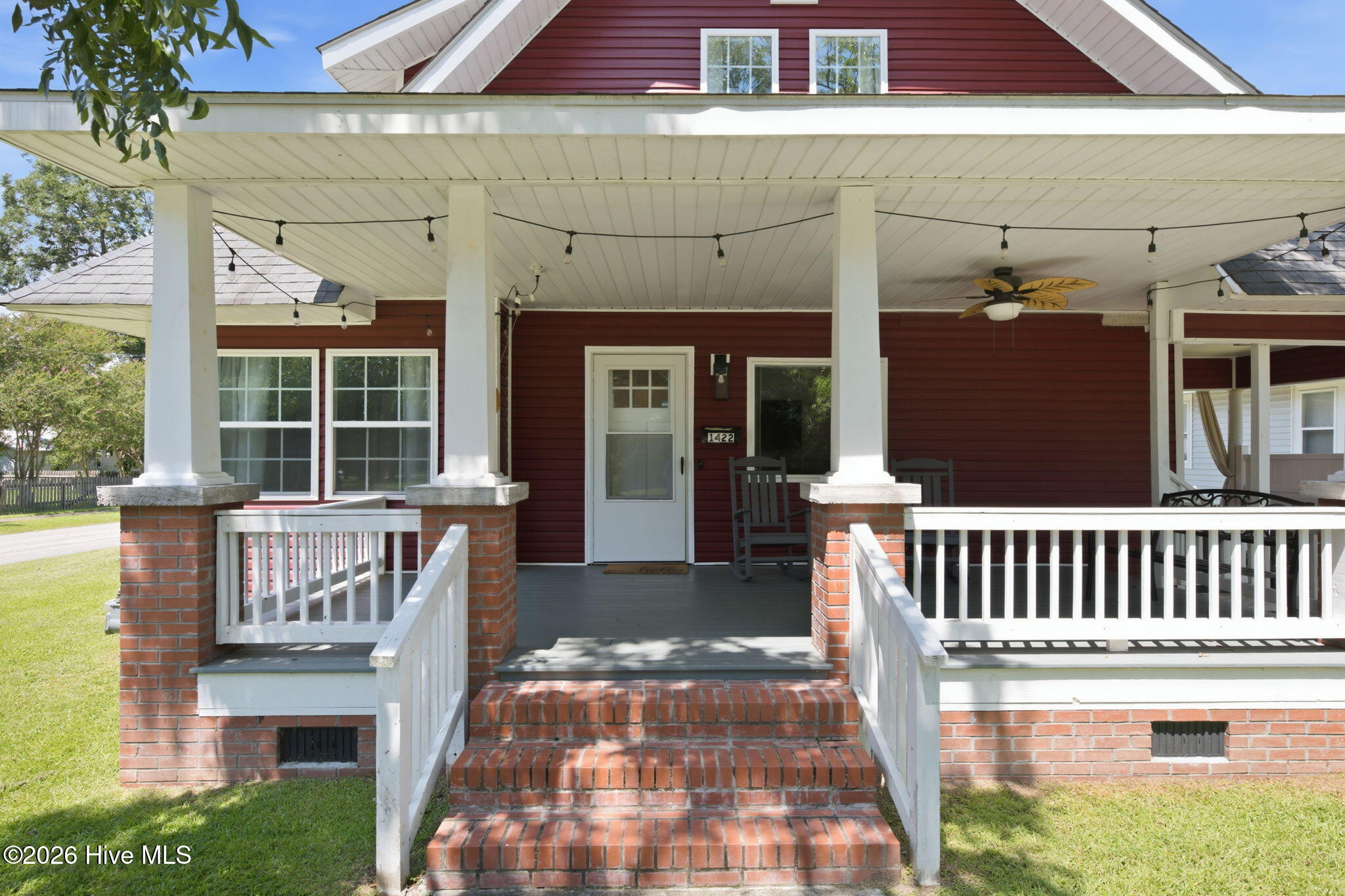 Red-sided home with a broad covered porch, white railings, and brick steps.