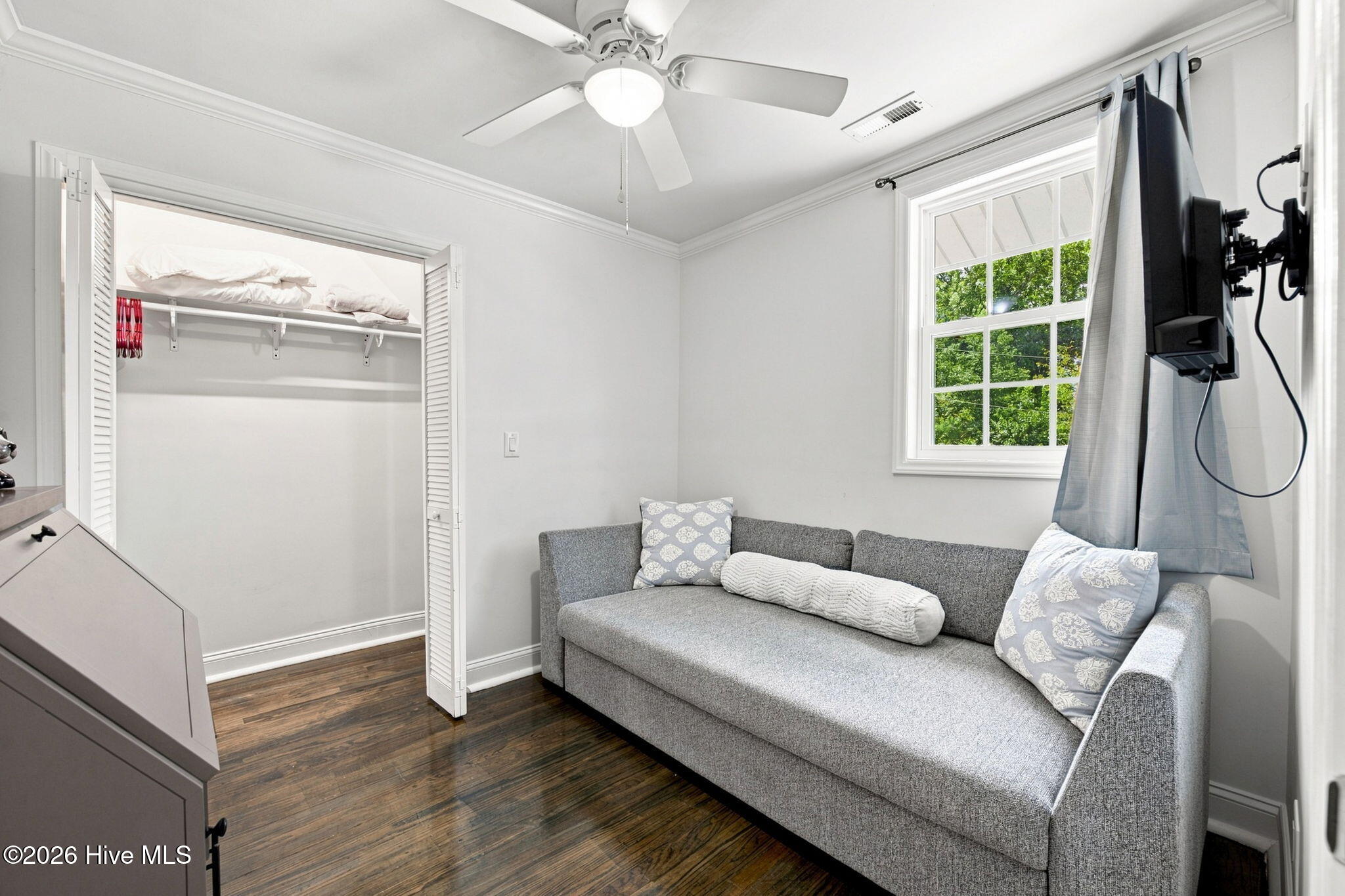 Bedroom with a gray sofa bed, open closet, and window overlooking trees.