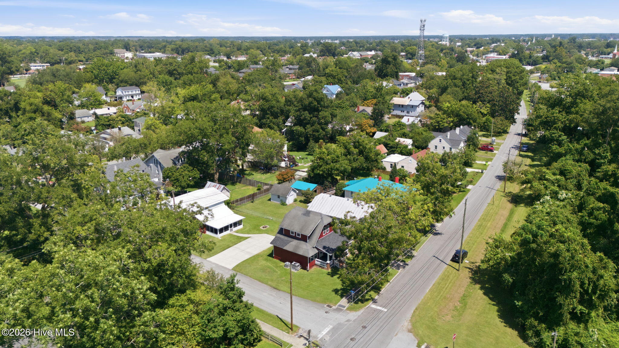 Aerial view of a red house amid leafy homes, with a road running alongside the neighborhood.