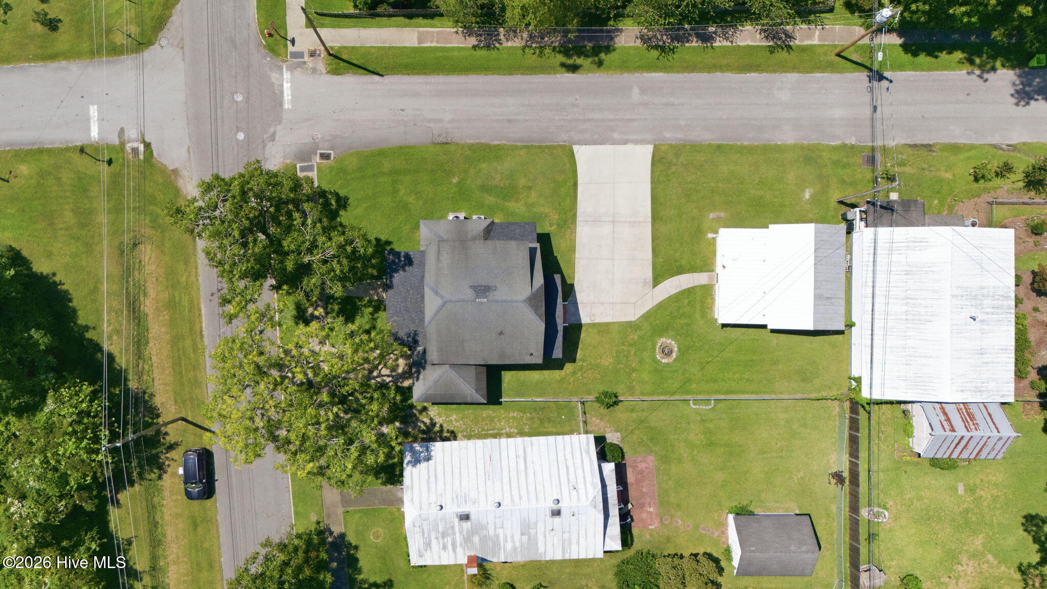 Aerial view of a dark-roofed house, broad lawn, and long driveway beside a residential street.