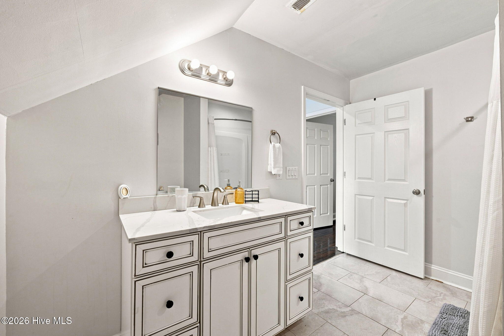 Bathroom with a paneled white vanity, marble-look countertop, large mirror, and light tile floor.
