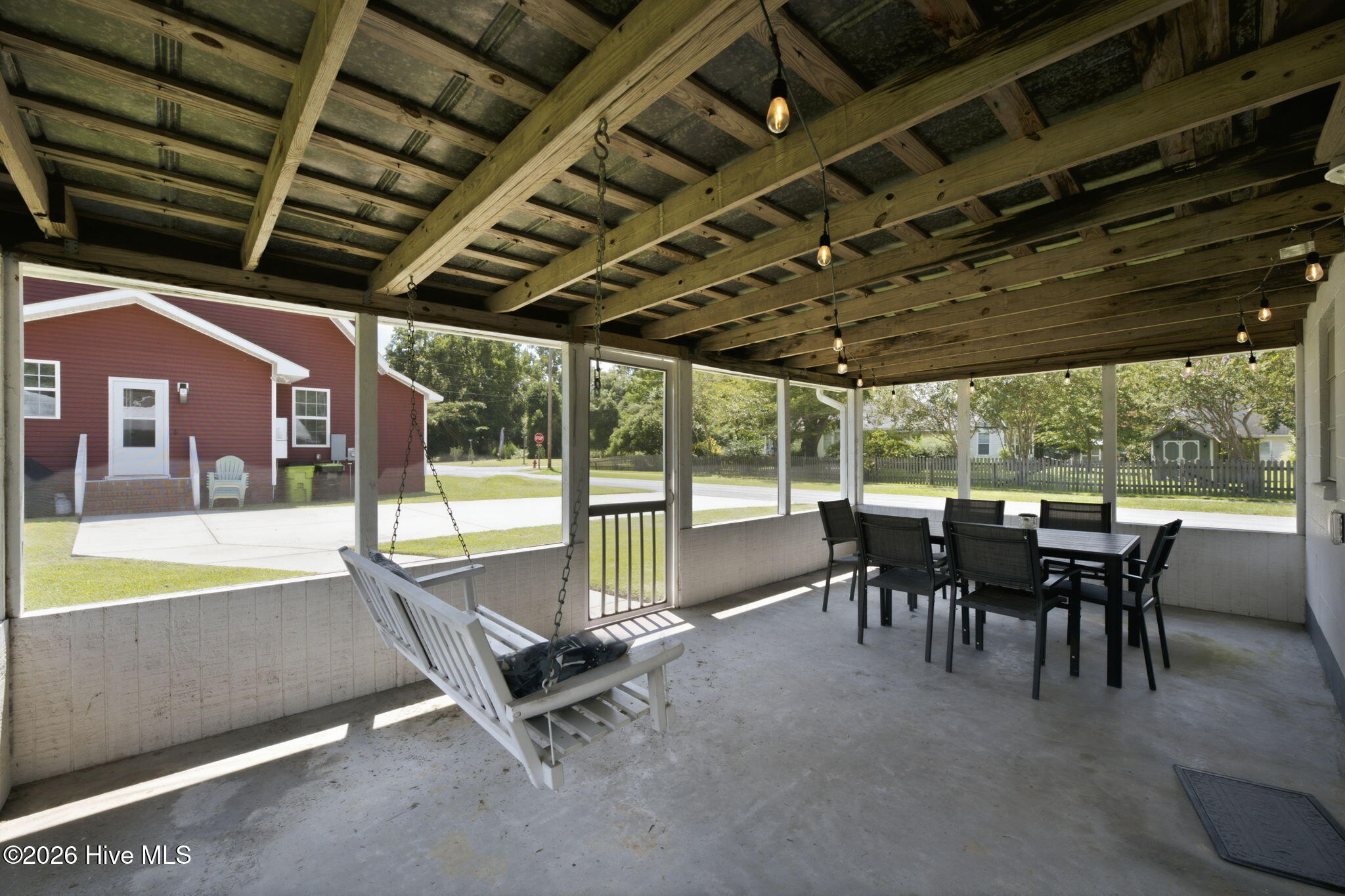 Covered porch with a hanging swing, string lights, and outdoor dining set.